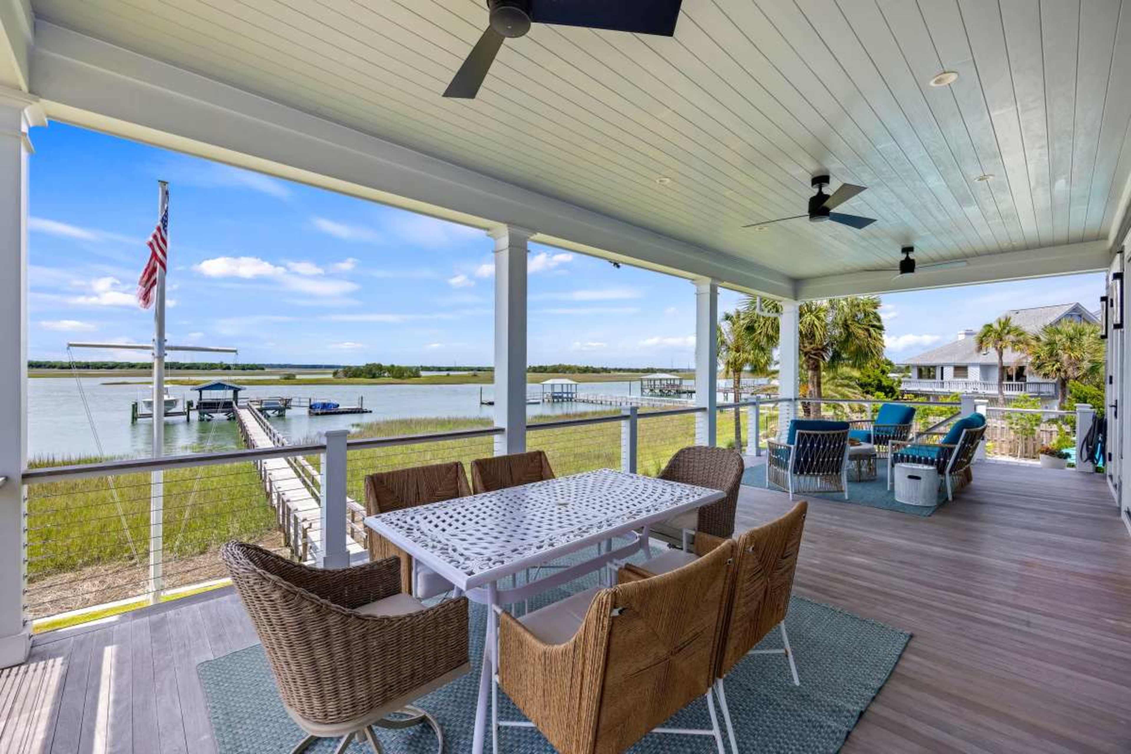 The image shows a covered patio with a dining table and chairs overlooking a body of water and a boat dock.