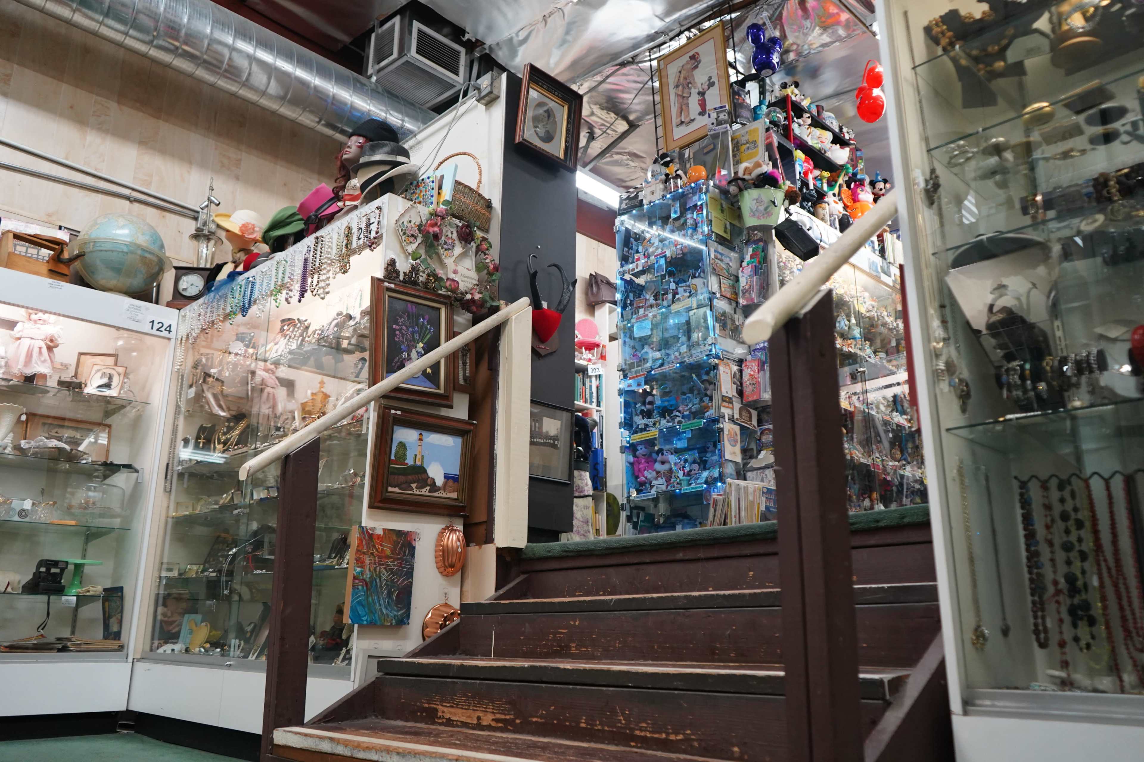 The image shows a staircase leading up to a display area filled with various items, including jewelry, collectibles, and decorative pieces, situated in an indoor space.