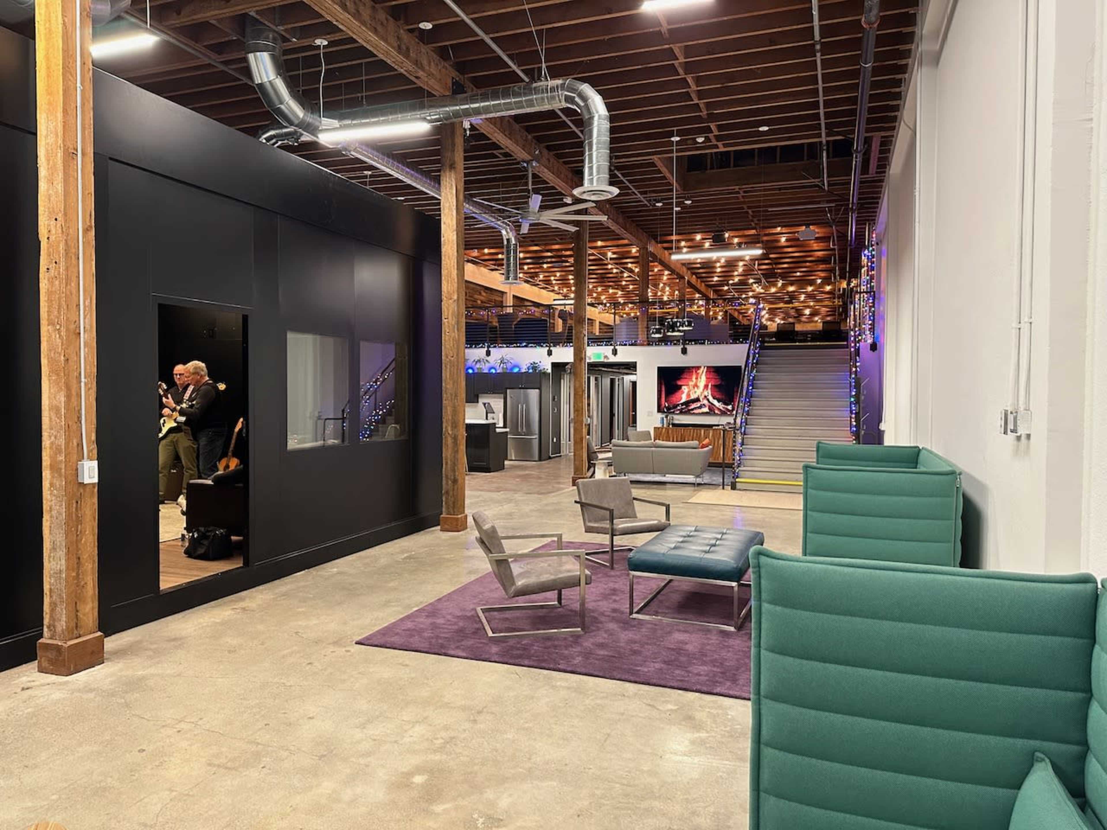 A spacious office area featuring a lounge space with green chairs, a purple rug, and an adjacent open area with modern furnishings and a staircase leading to a different level.