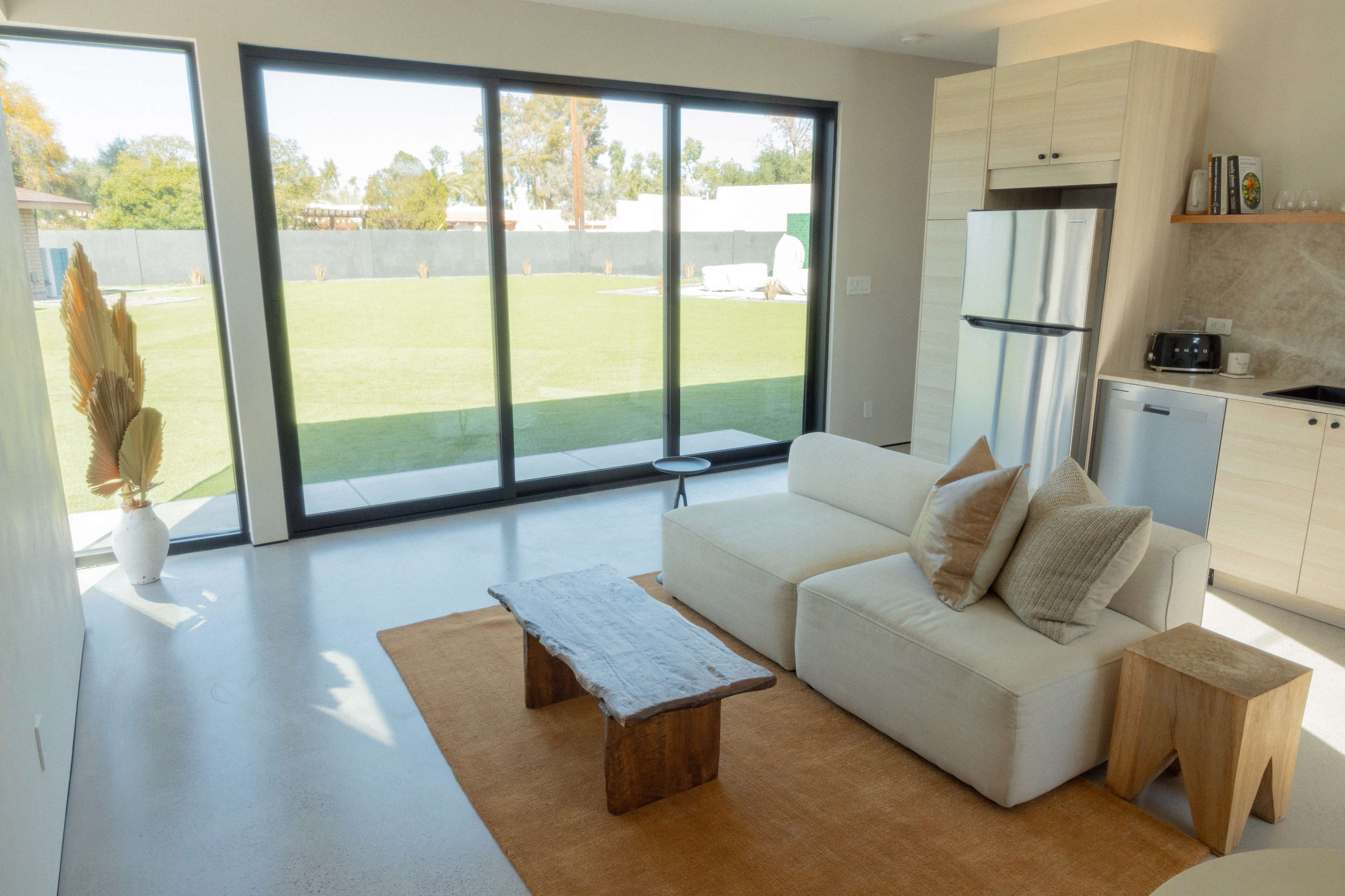 A modern living space with a white sofa, a wooden coffee table, and large glass doors leading to a green outdoor area.