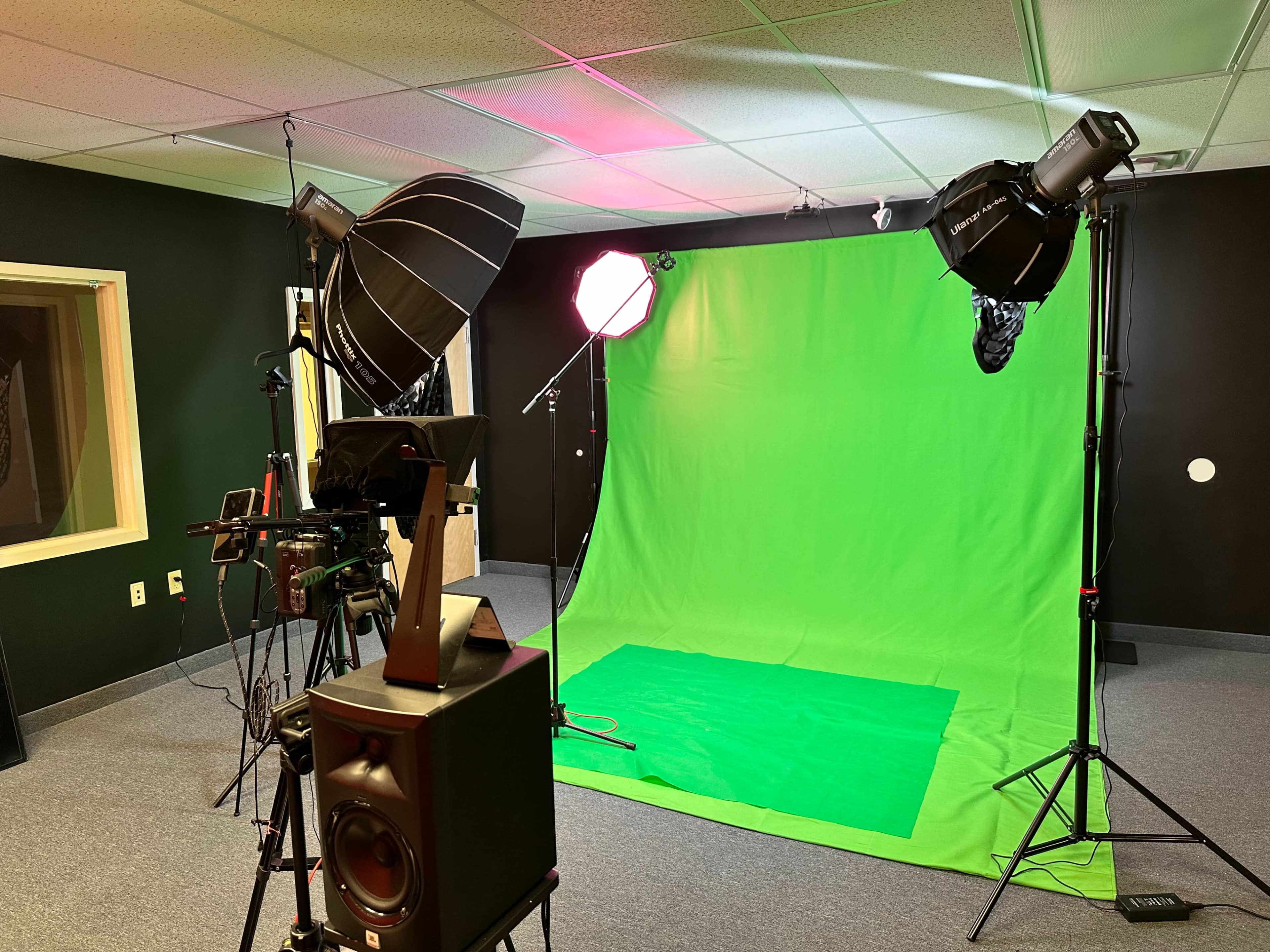 The image shows a photography studio setup featuring a green screen, lighting equipment, and cameras arranged in the space.