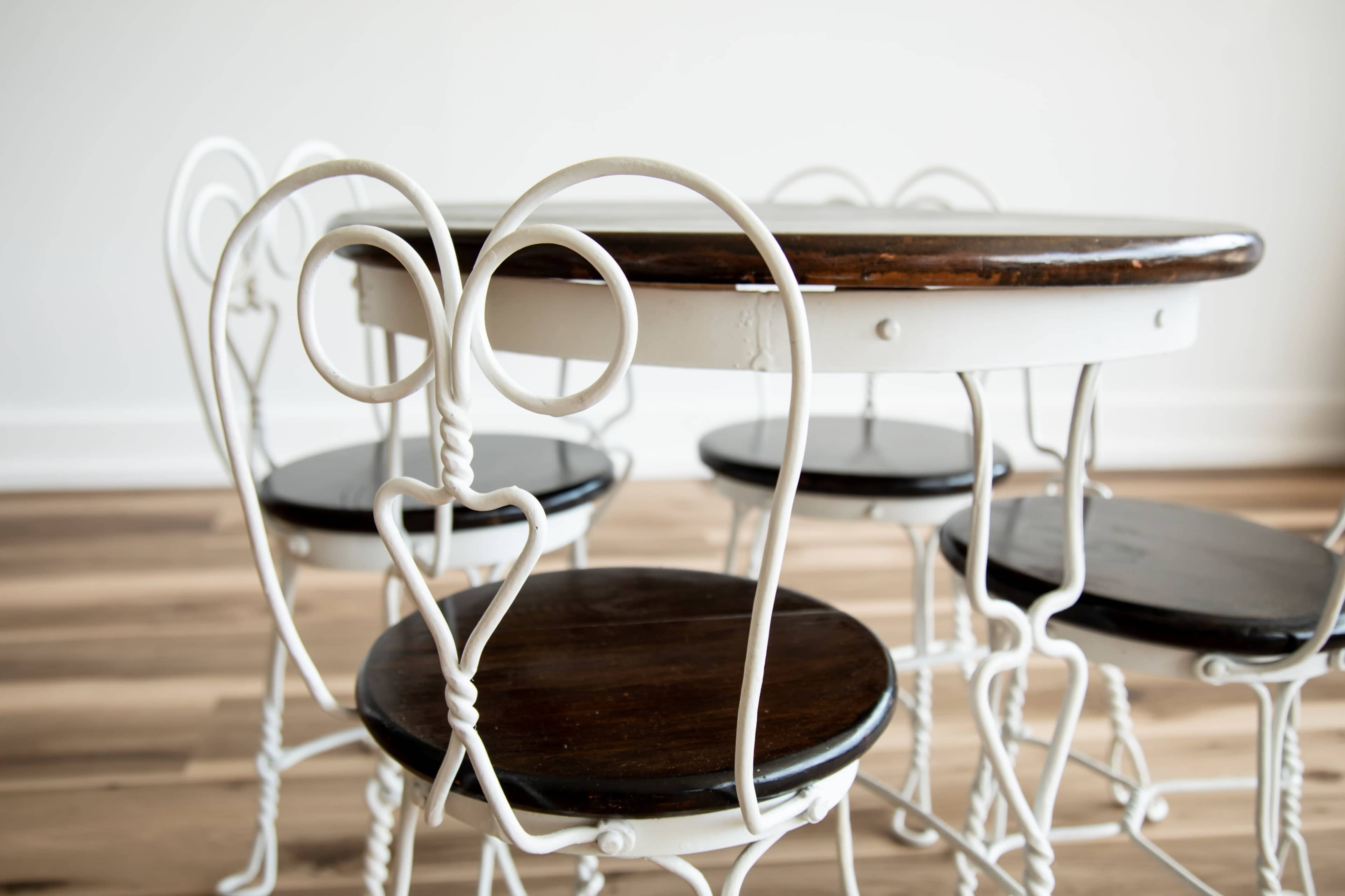 The image features a round wooden table surrounded by white iron chairs with circular backs and dark wooden seats.