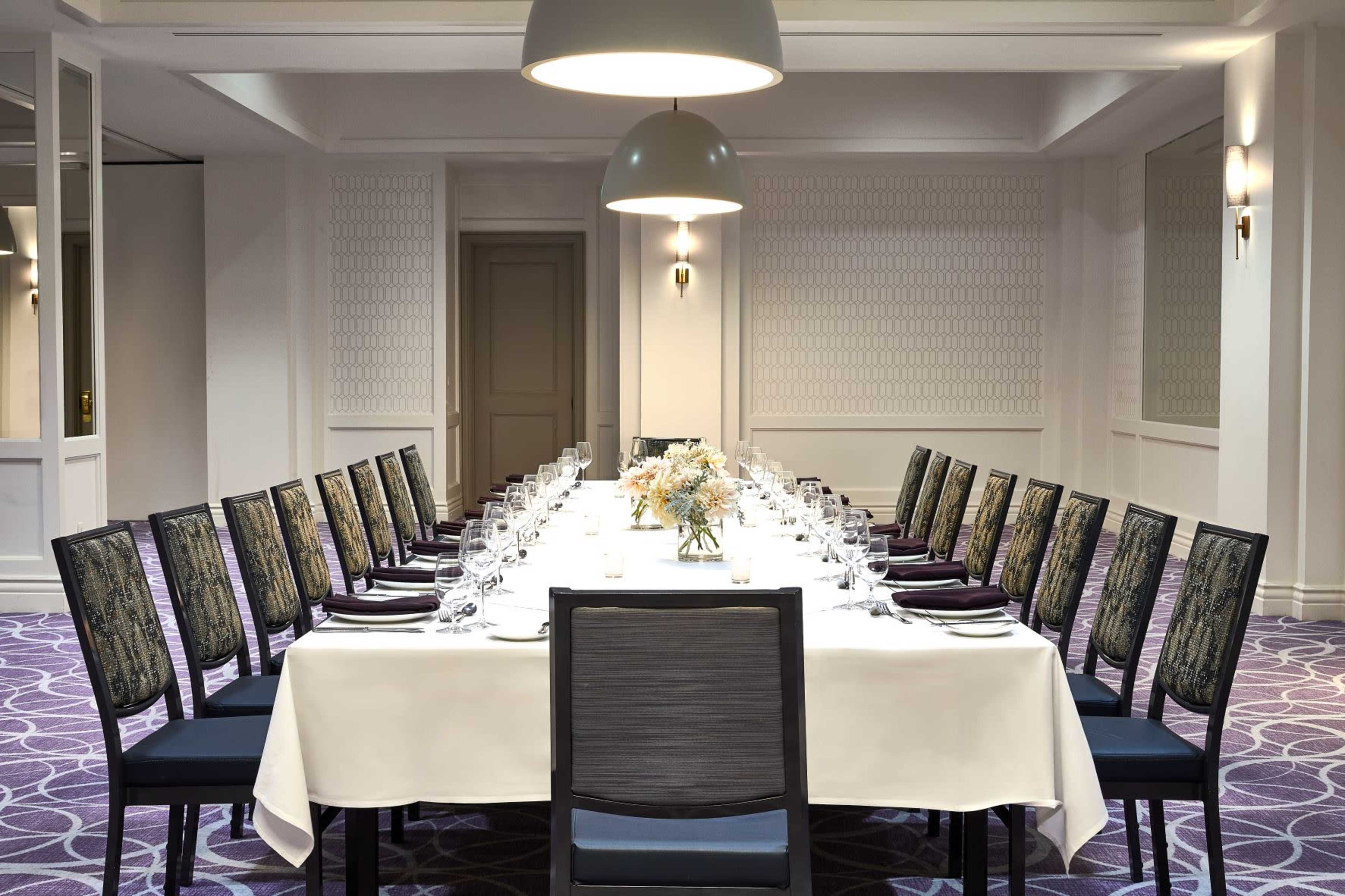 A long dining table is set with glasses and decorations, surrounded by chairs in a well-lit room.