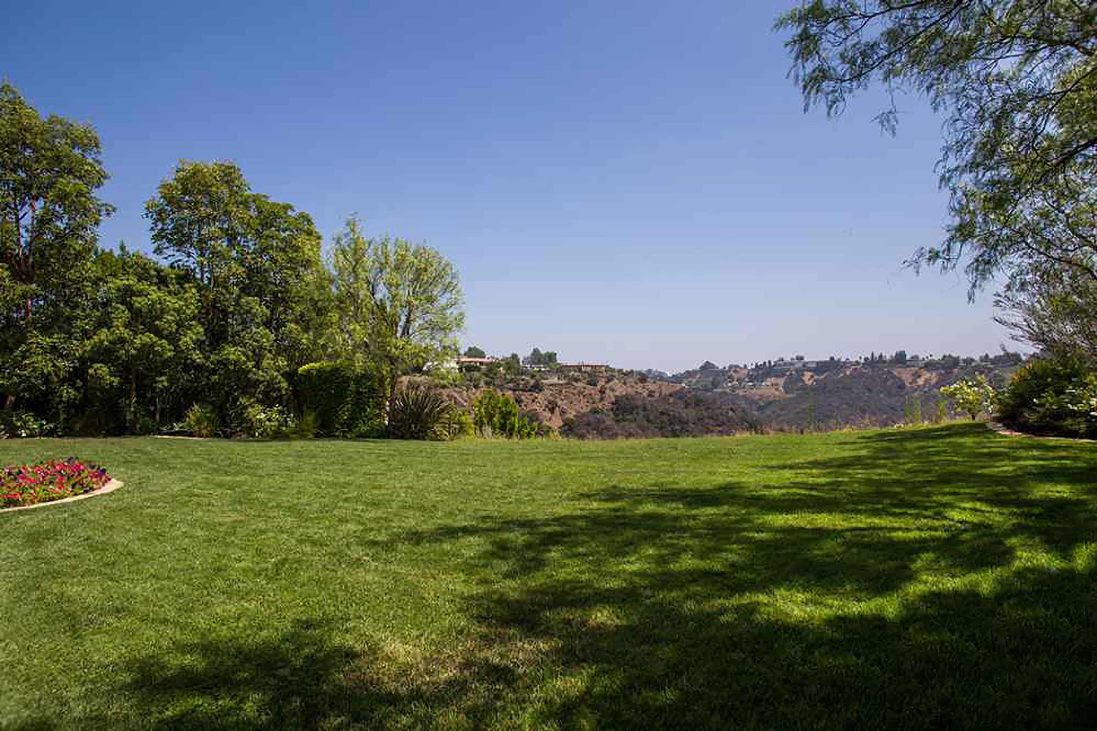A green lawn with trees and a distant hillside under a clear blue sky.