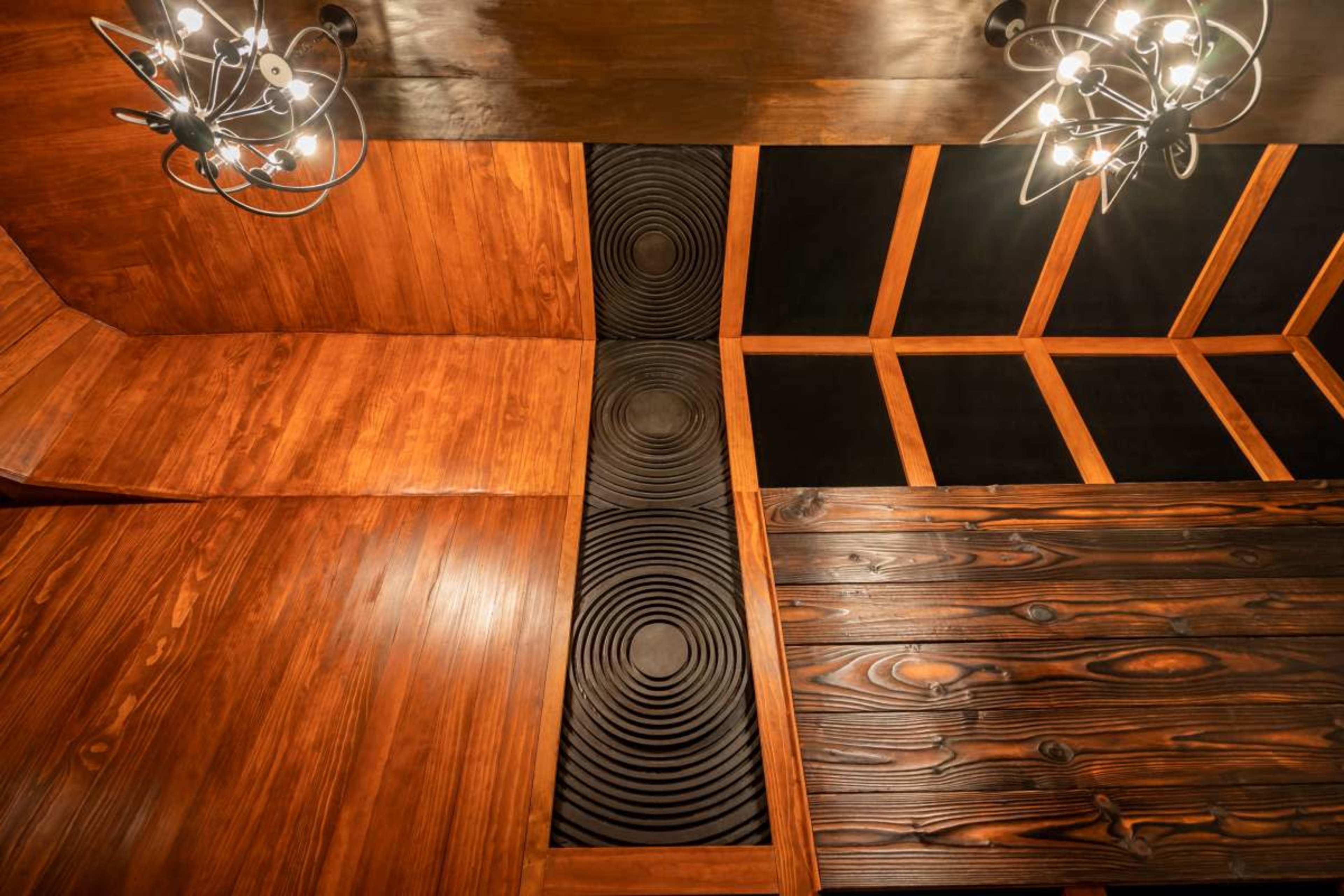 The image shows a wooden ceiling with dark panels featuring circular designs, illuminated by modern light fixtures.