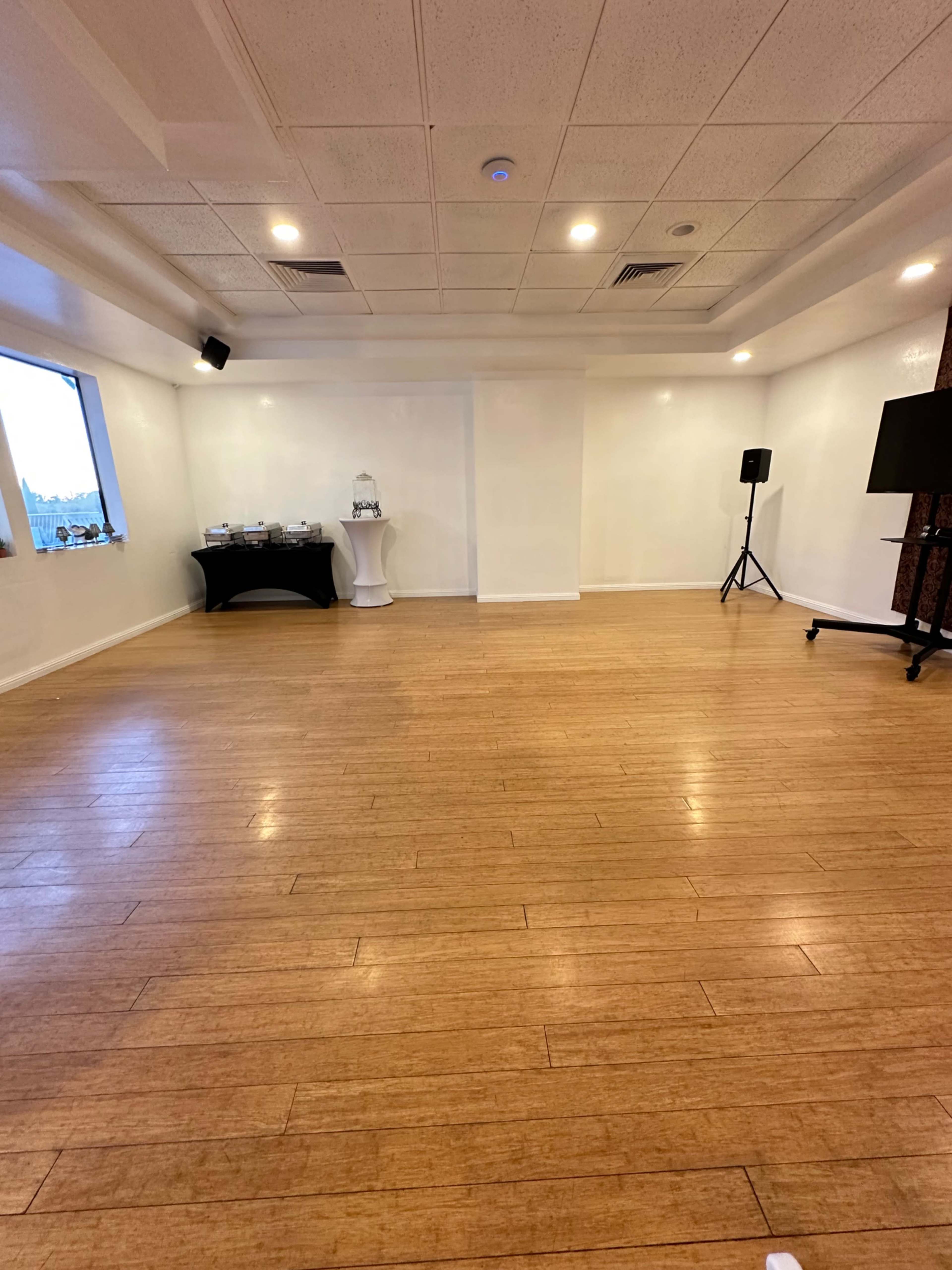 The image shows an empty interior space with wooden flooring, white walls, and a table set up on one side.