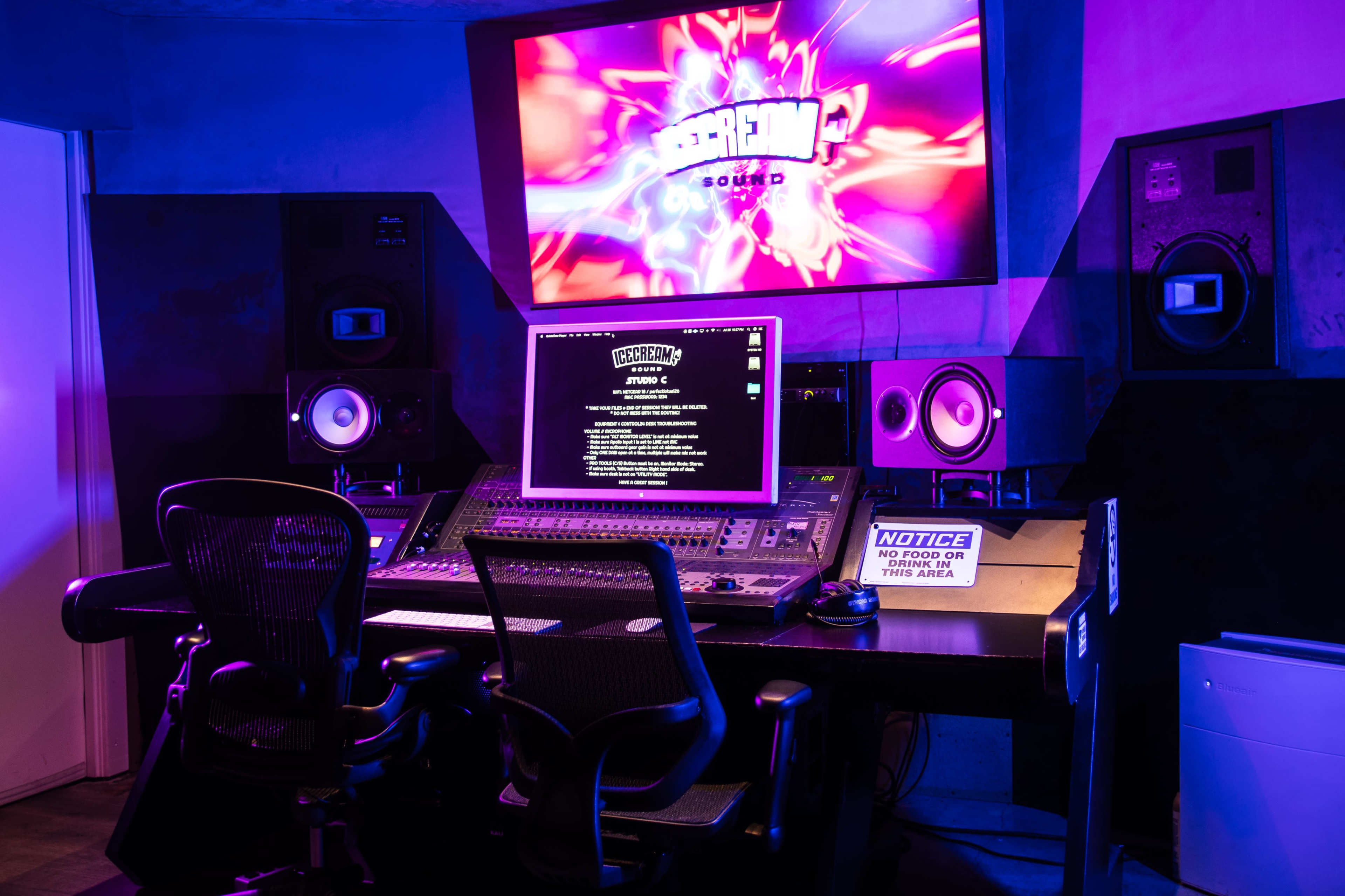 A modern recording studio featuring a control panel with monitors, speakers, and ambient lighting.