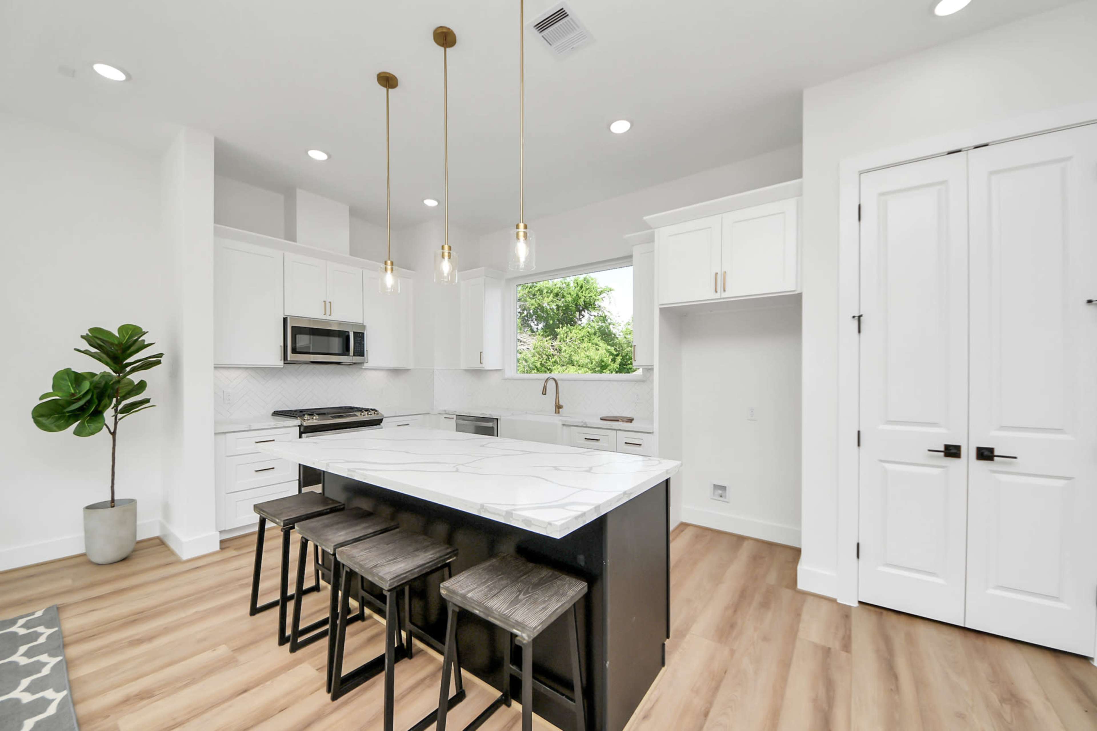 The image shows a modern kitchen with a central island, white cabinets, a marble countertop, and pendant lighting.