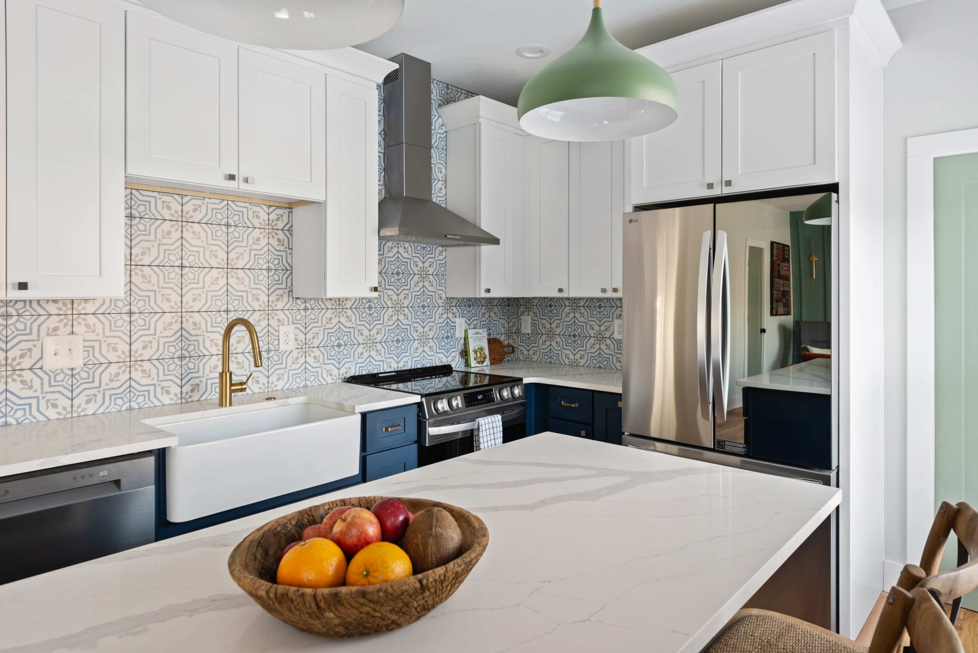 A modern kitchen with white cabinets, a blue island, and a bowl of fruit on the countertop.