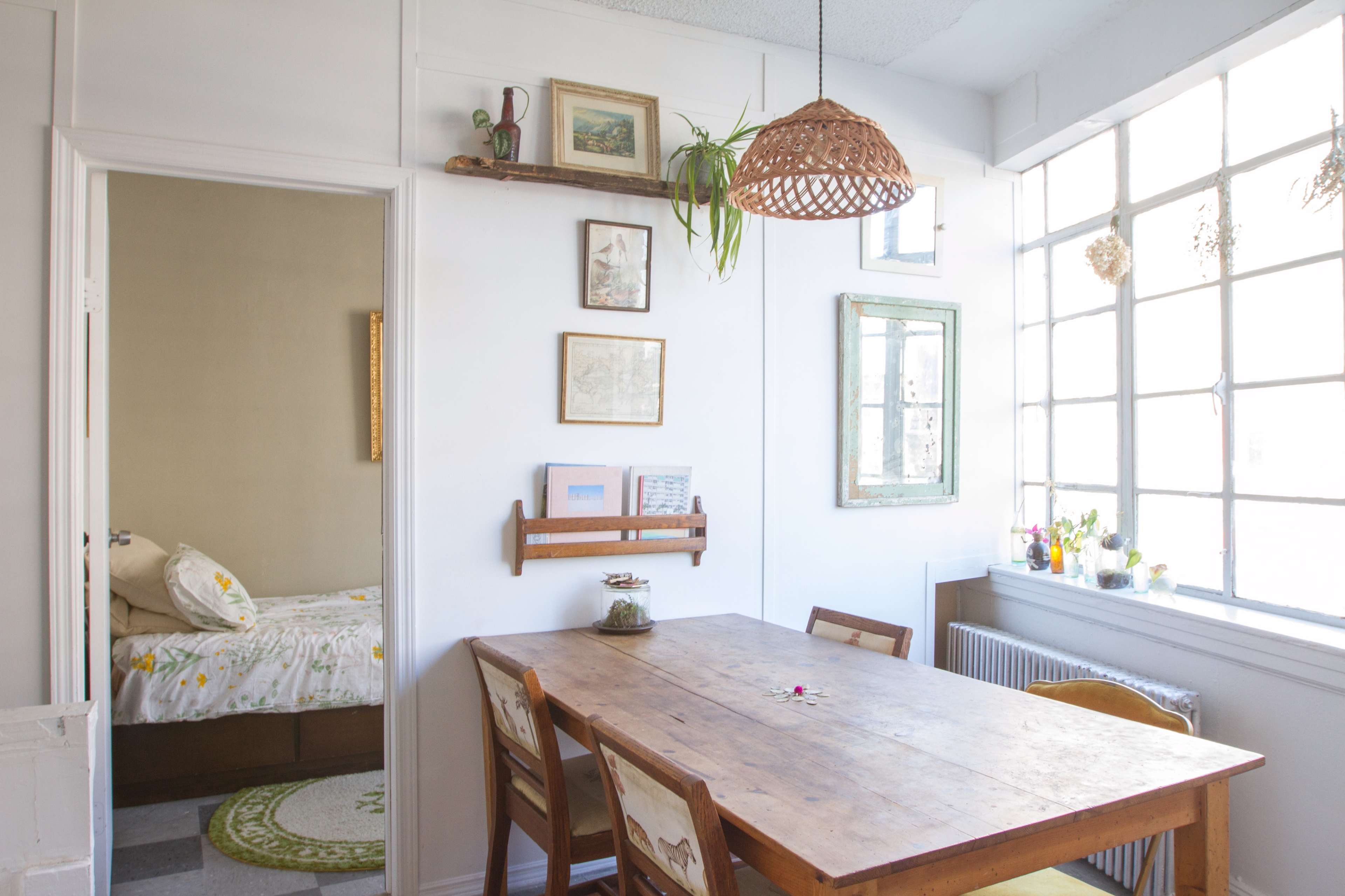 A dining area features a wooden table surrounded by chairs, with framed artwork on the walls and a large window providing natural light.