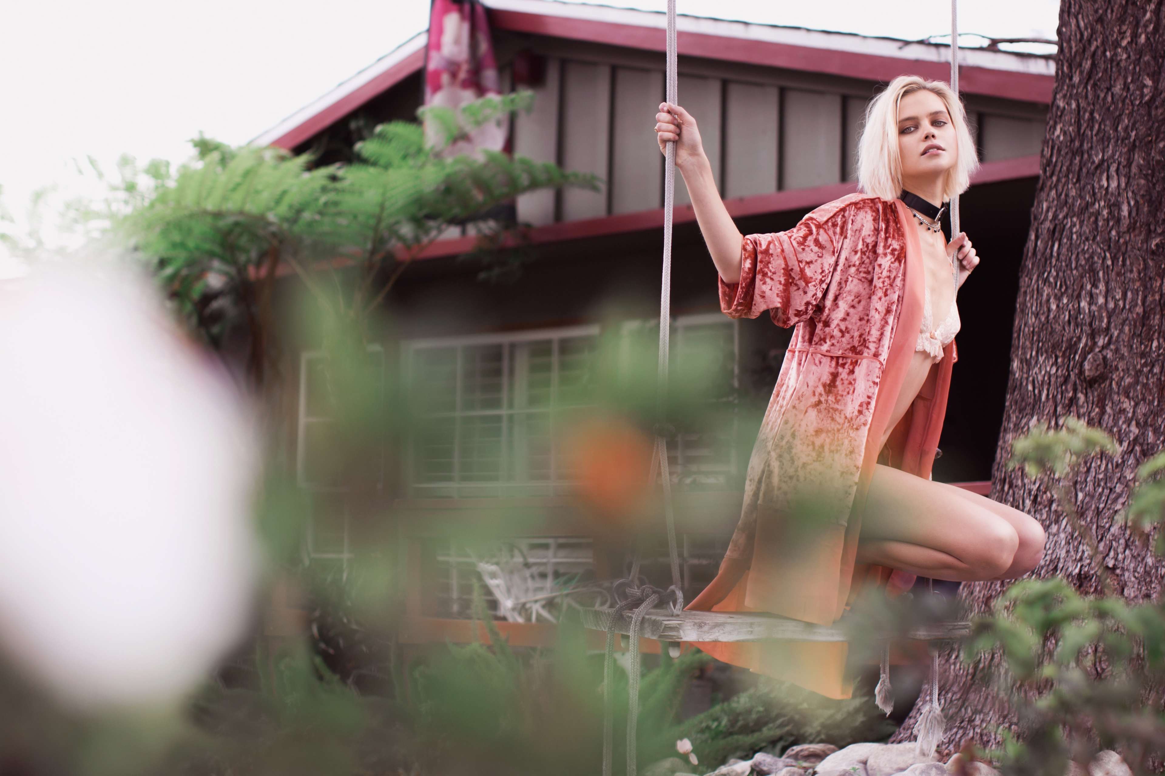 A person in a velvet cloak sits on a swing in a garden area near a house.