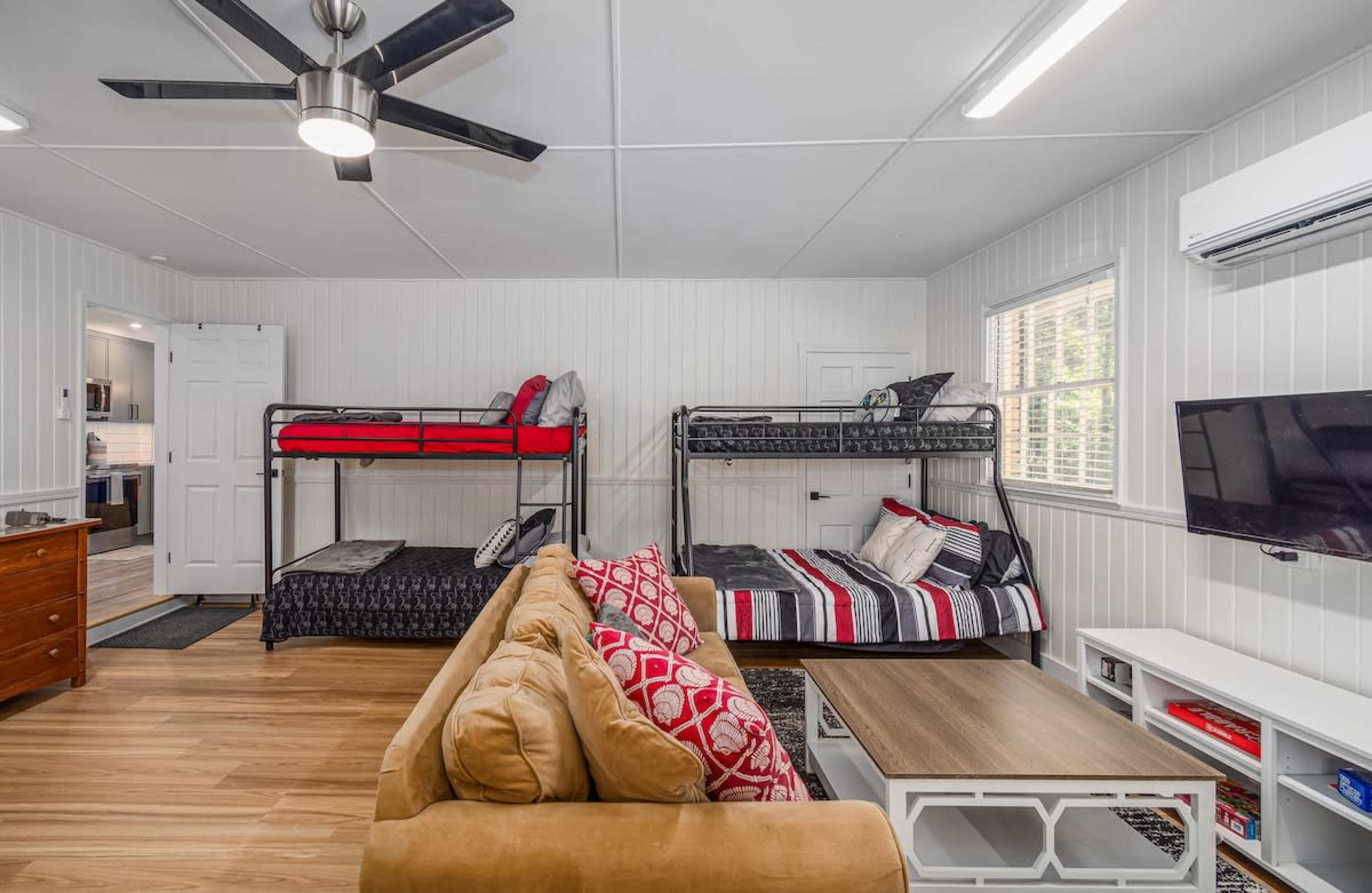The image shows a room with two bunk beds and a couch, along with a coffee table and a wall-mounted television.