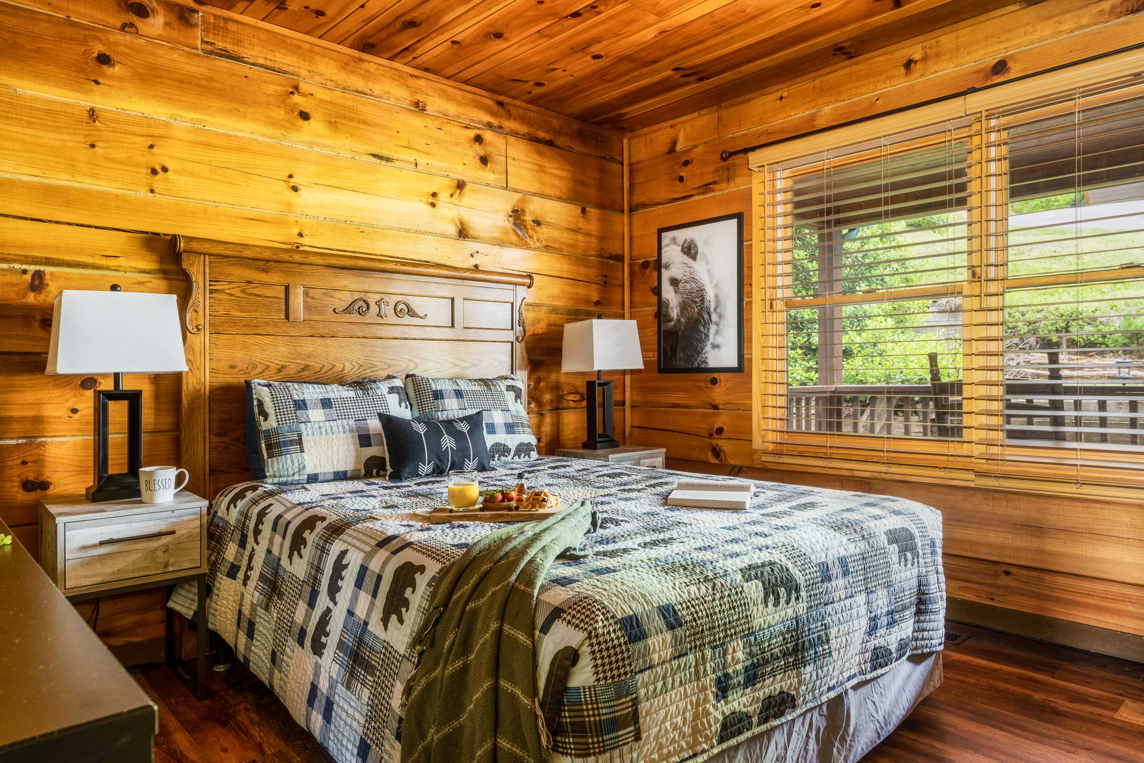 A cozy bedroom featuring a wooden bed frame with a checkered bedspread, two bedside lamps, and a window with wooden blinds.