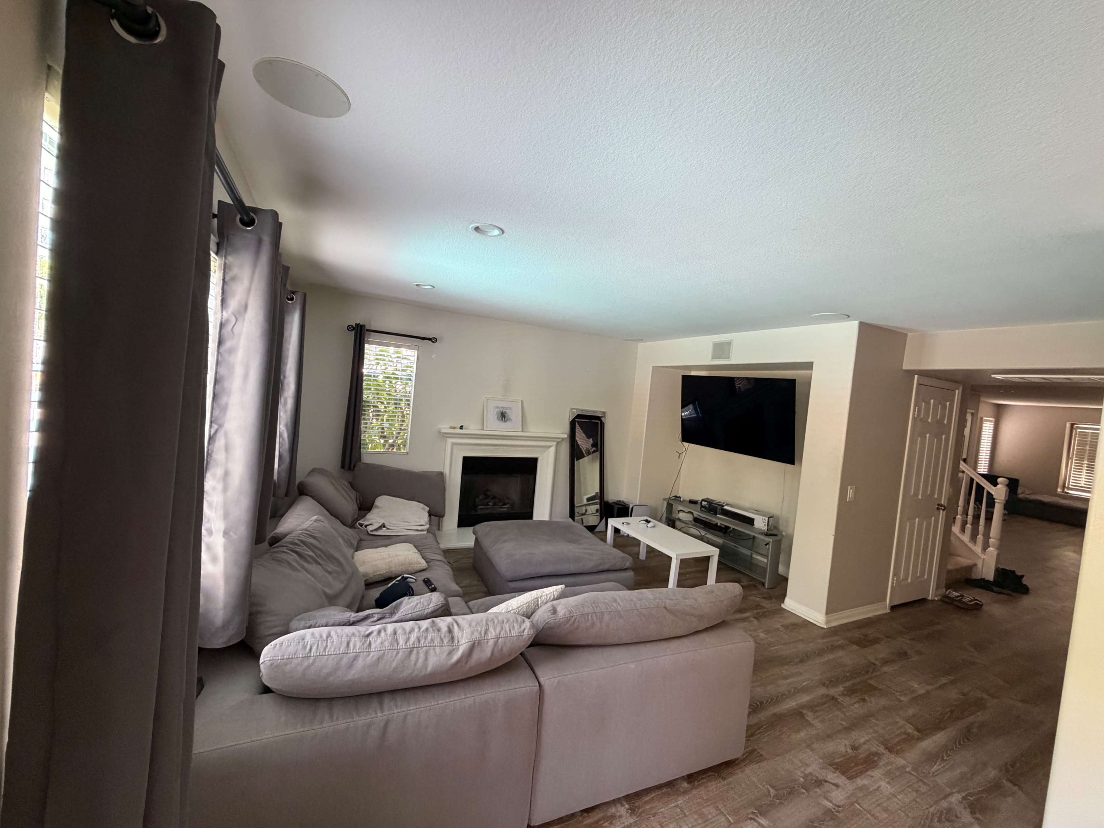 The image shows a living room featuring a large sectional sofa, a coffee table, a fireplace, and a television mounted on the wall.