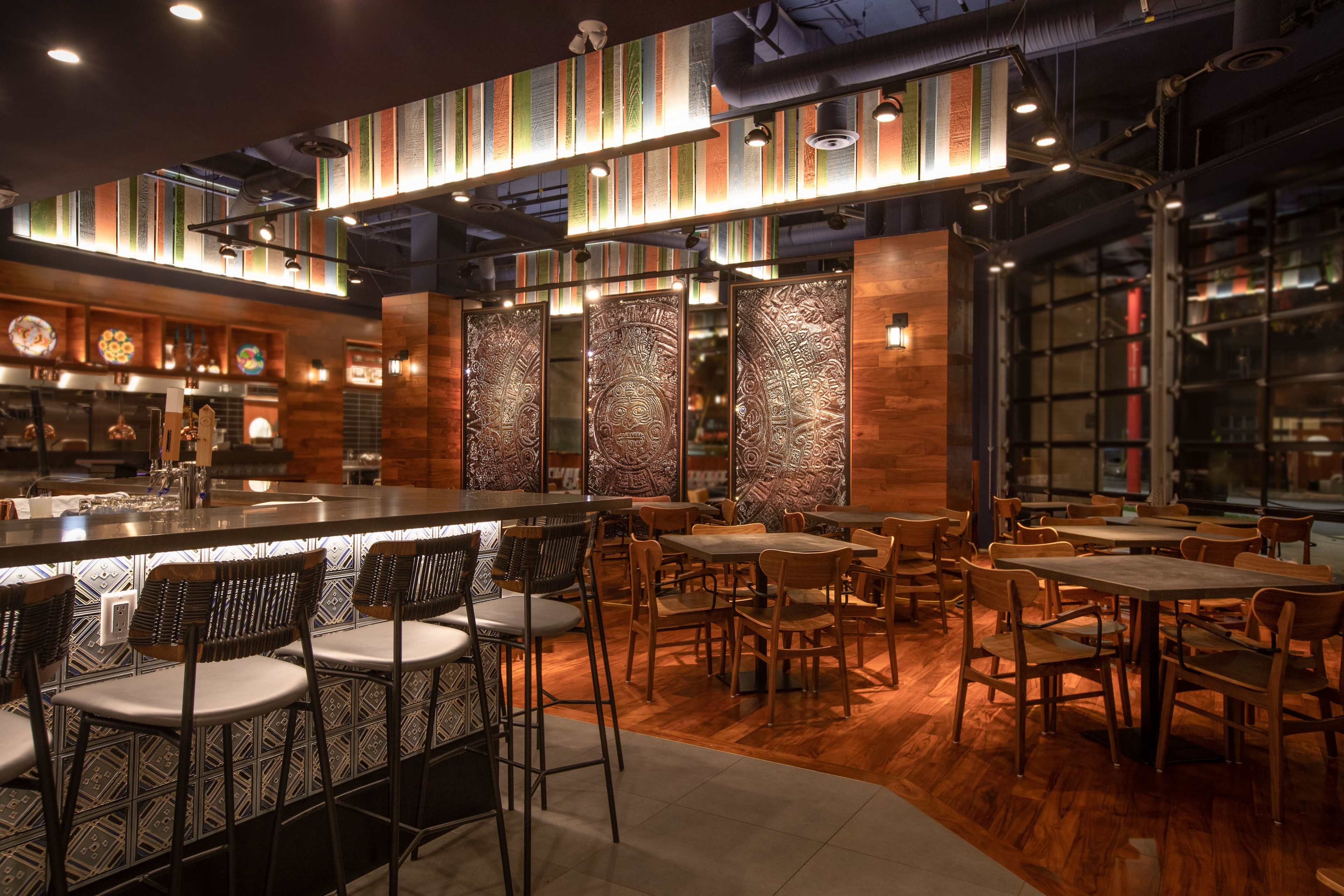 A stylish restaurant interior featuring a curved bar, wooden furniture, decorative wall panels, and patterned overhead decor.