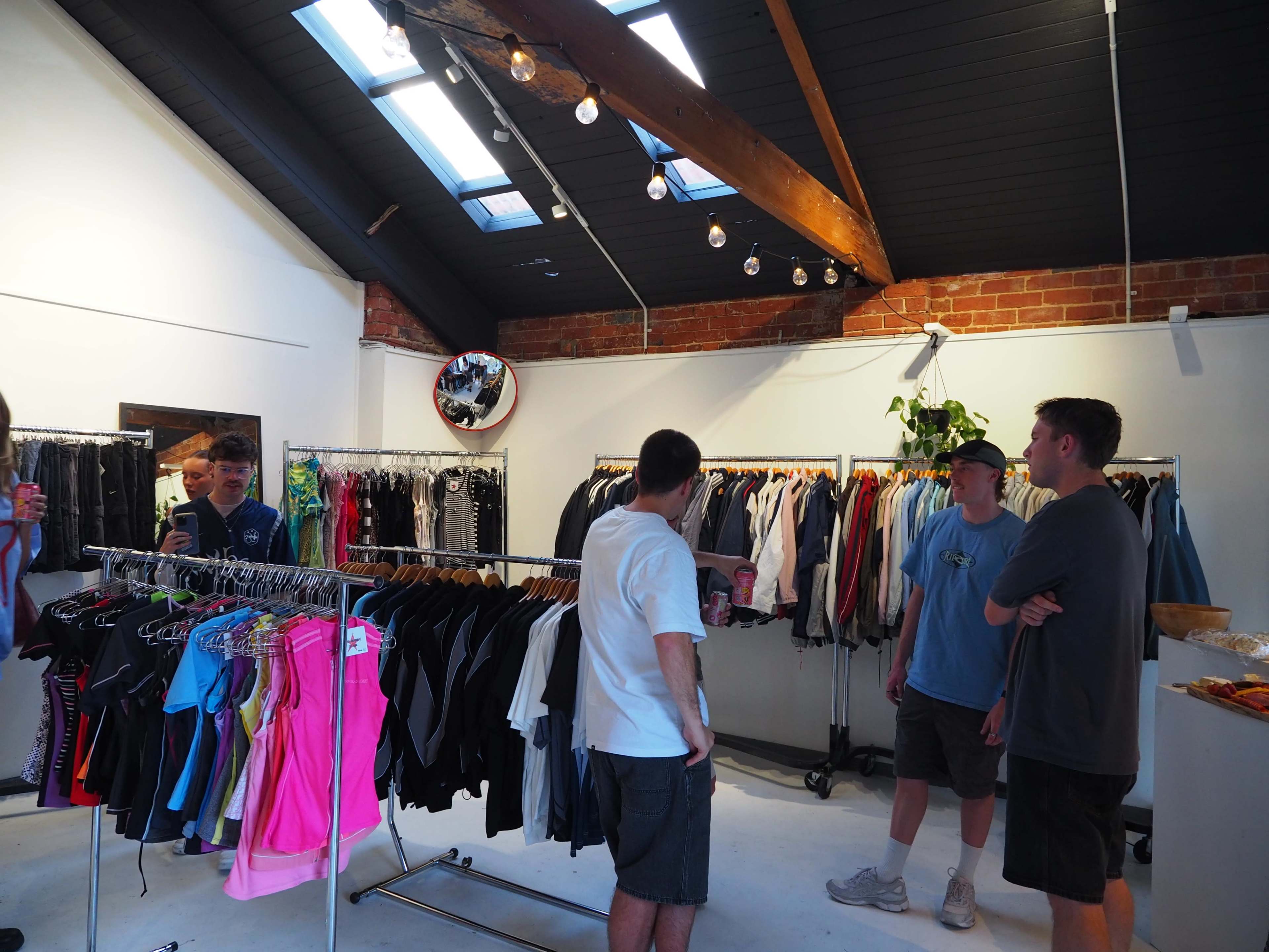 A group of four men converse in a clothing store featuring racks of colorful apparel and wooden beams above.