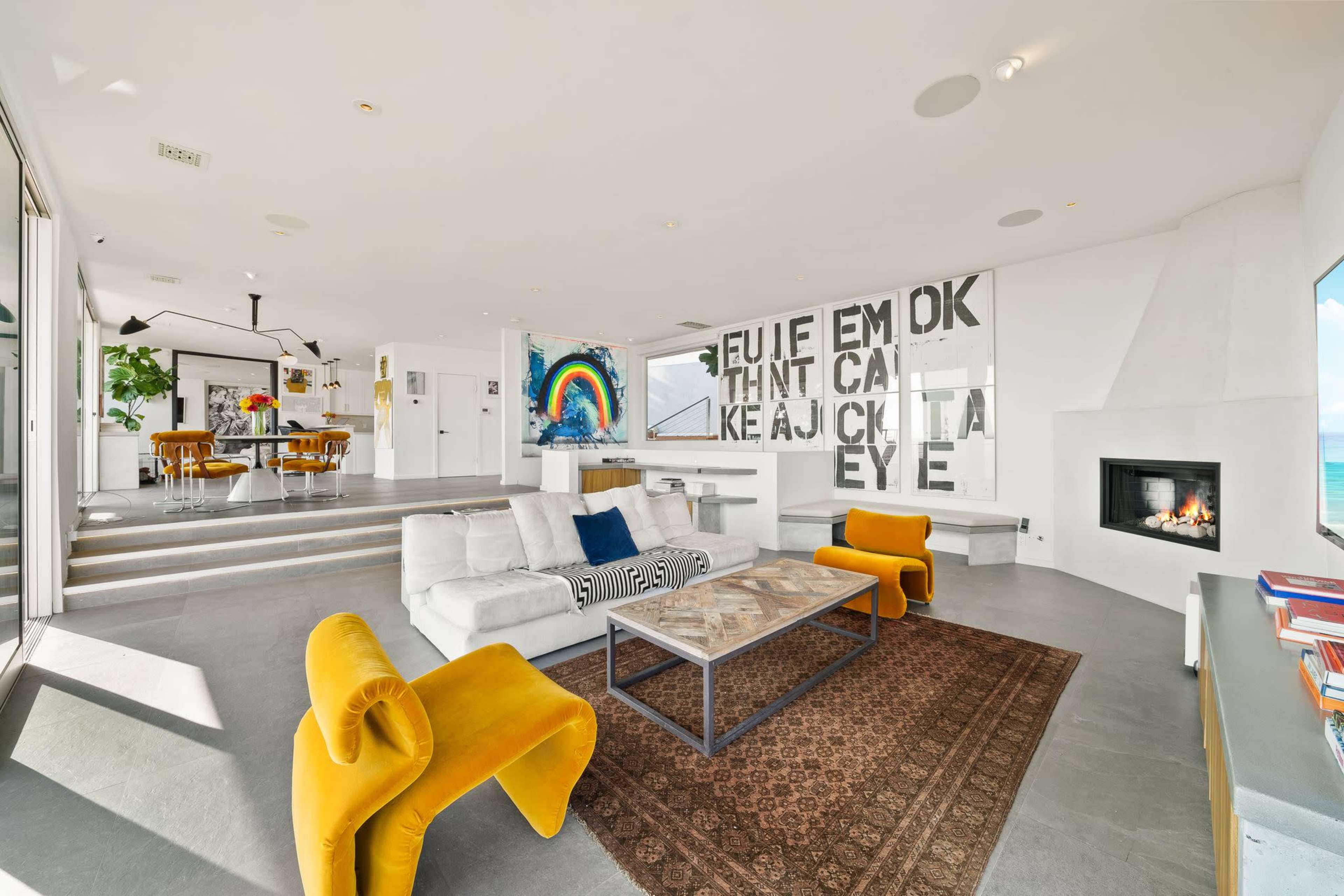 The image features a modern, open-plan living room with a fireplace, a large wall art display, and a dining area visible in the background.