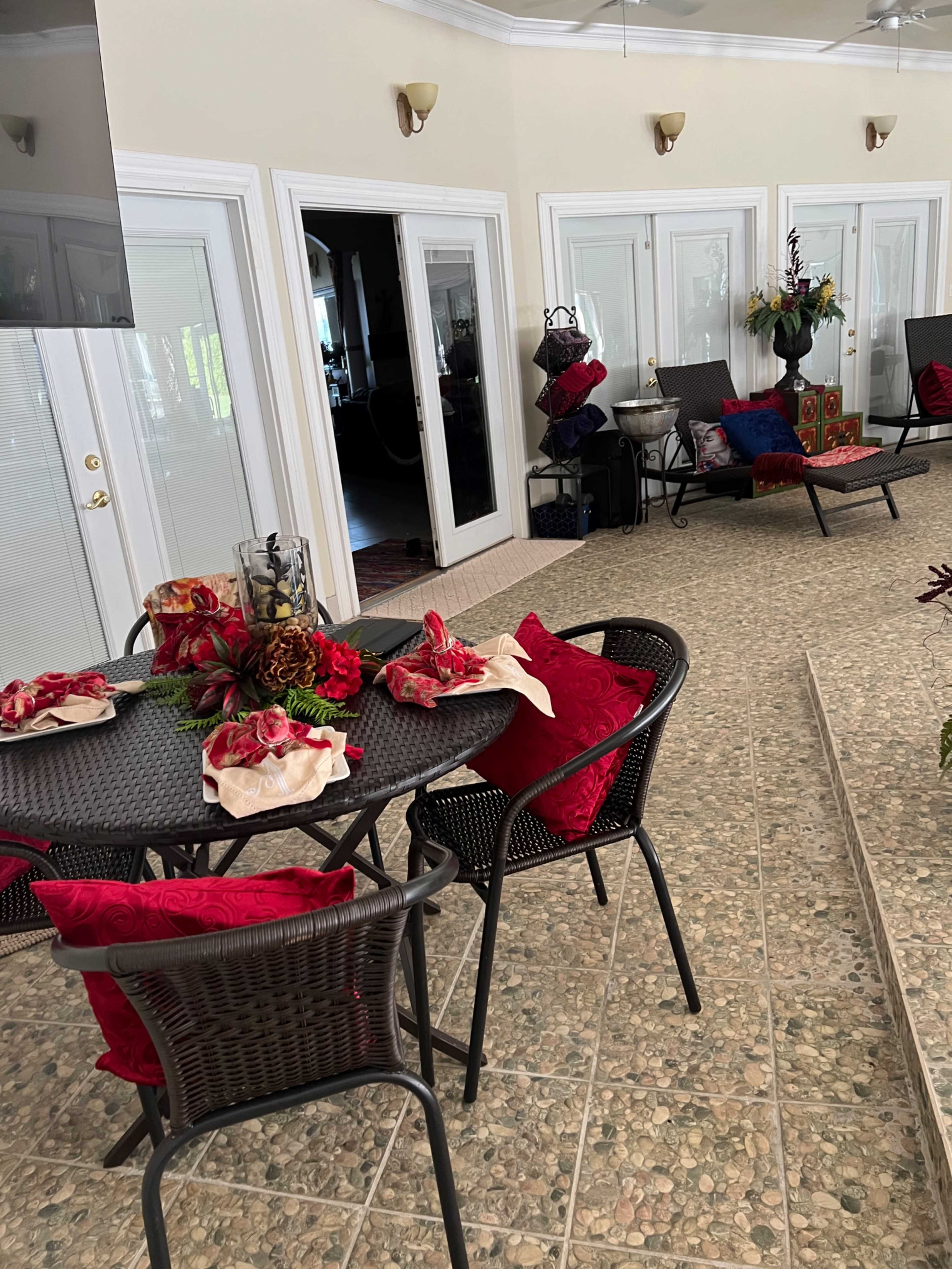 A spacious indoor area with a round table set with a floral centerpiece and chairs, along with a view of neighboring rooms through glass doors.