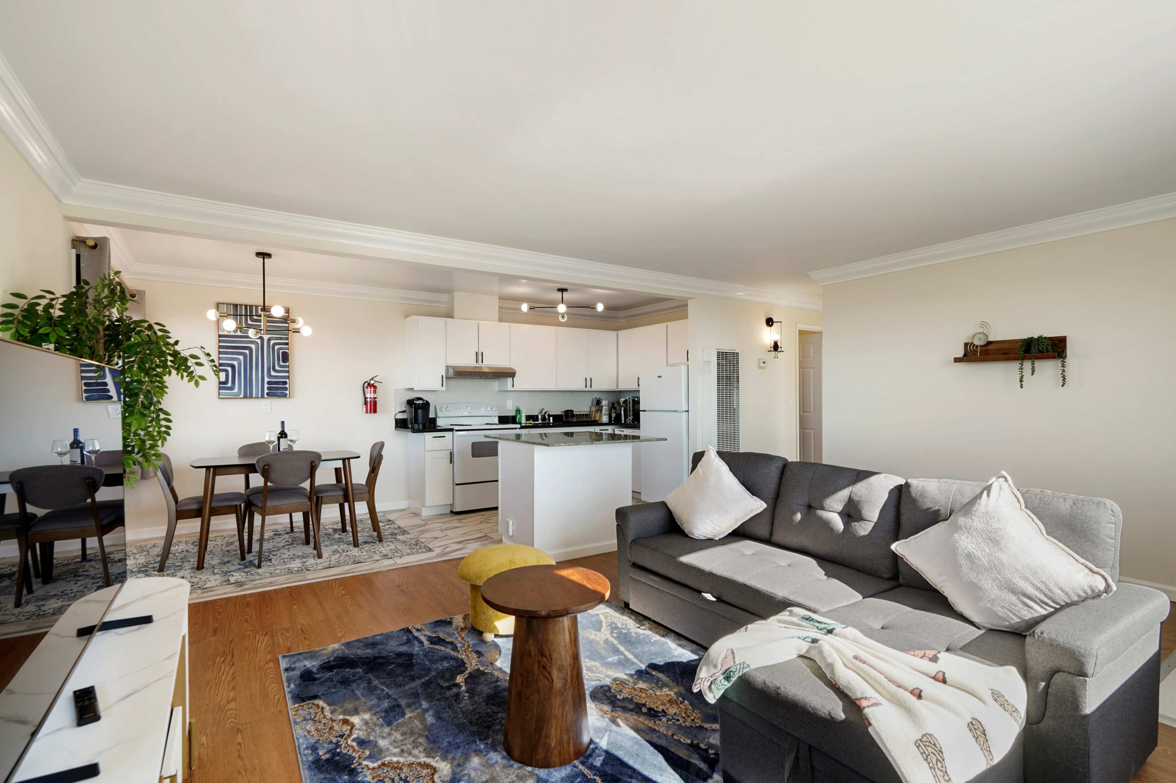 The image shows a modern living room with a gray sofa, a small wooden table, and a dining area featuring a round table and four chairs.