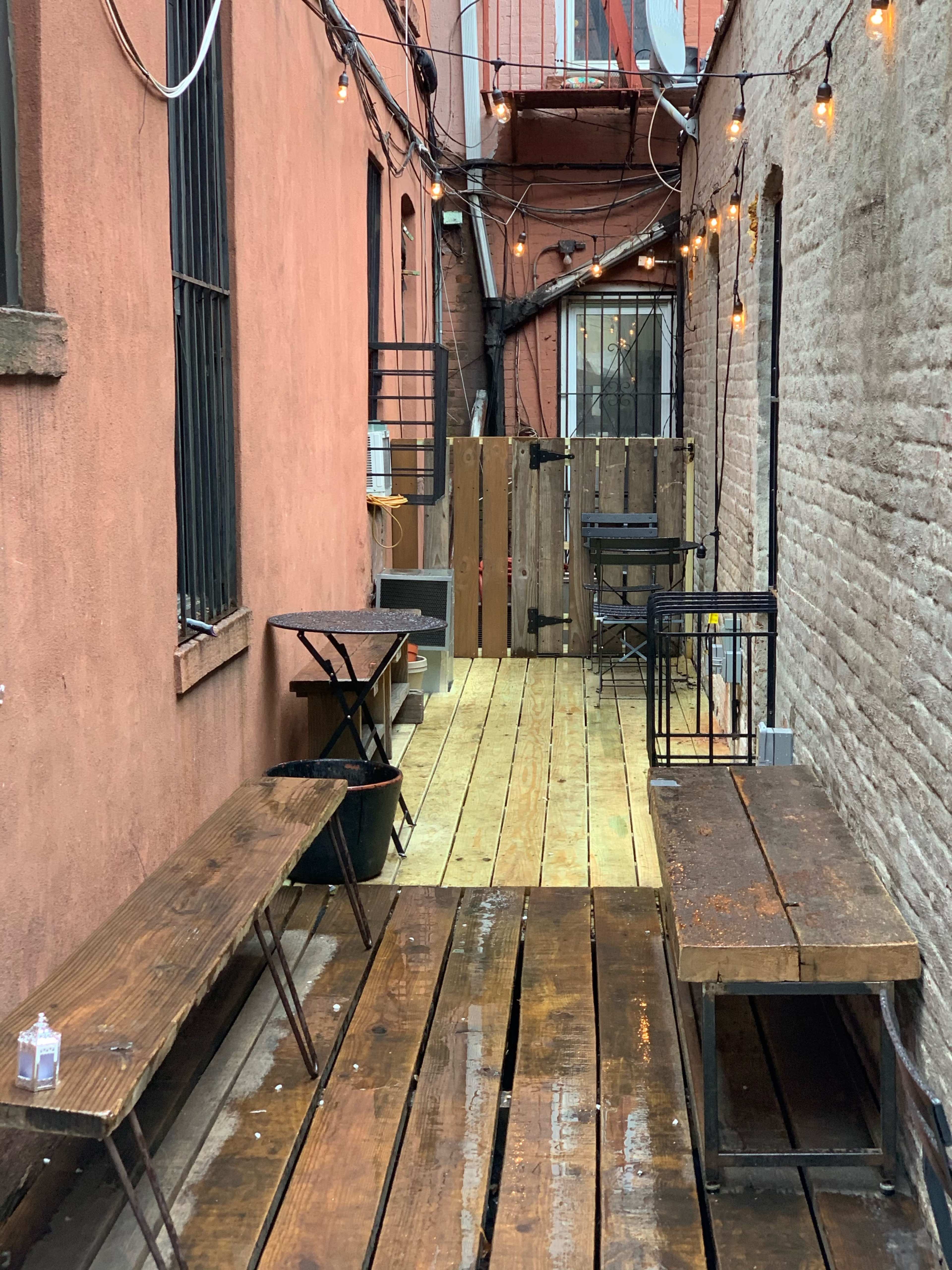 An alleyway with wooden flooring, two long benches, and strings of lights overhead.