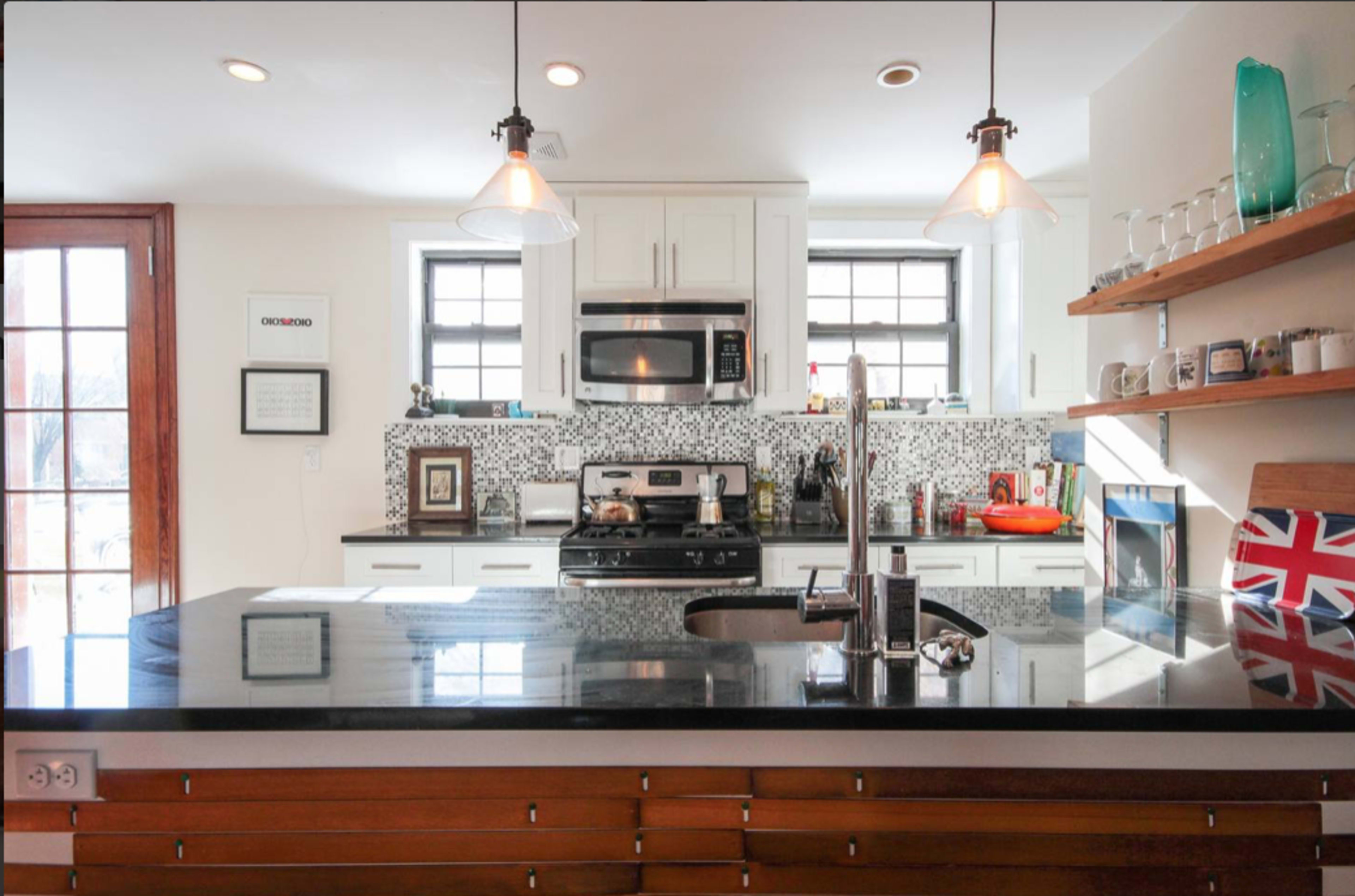 The kitchen features white cabinetry, a dark countertop, and modern appliances, with a striking patterned backsplash and wooden shelves displaying various items.