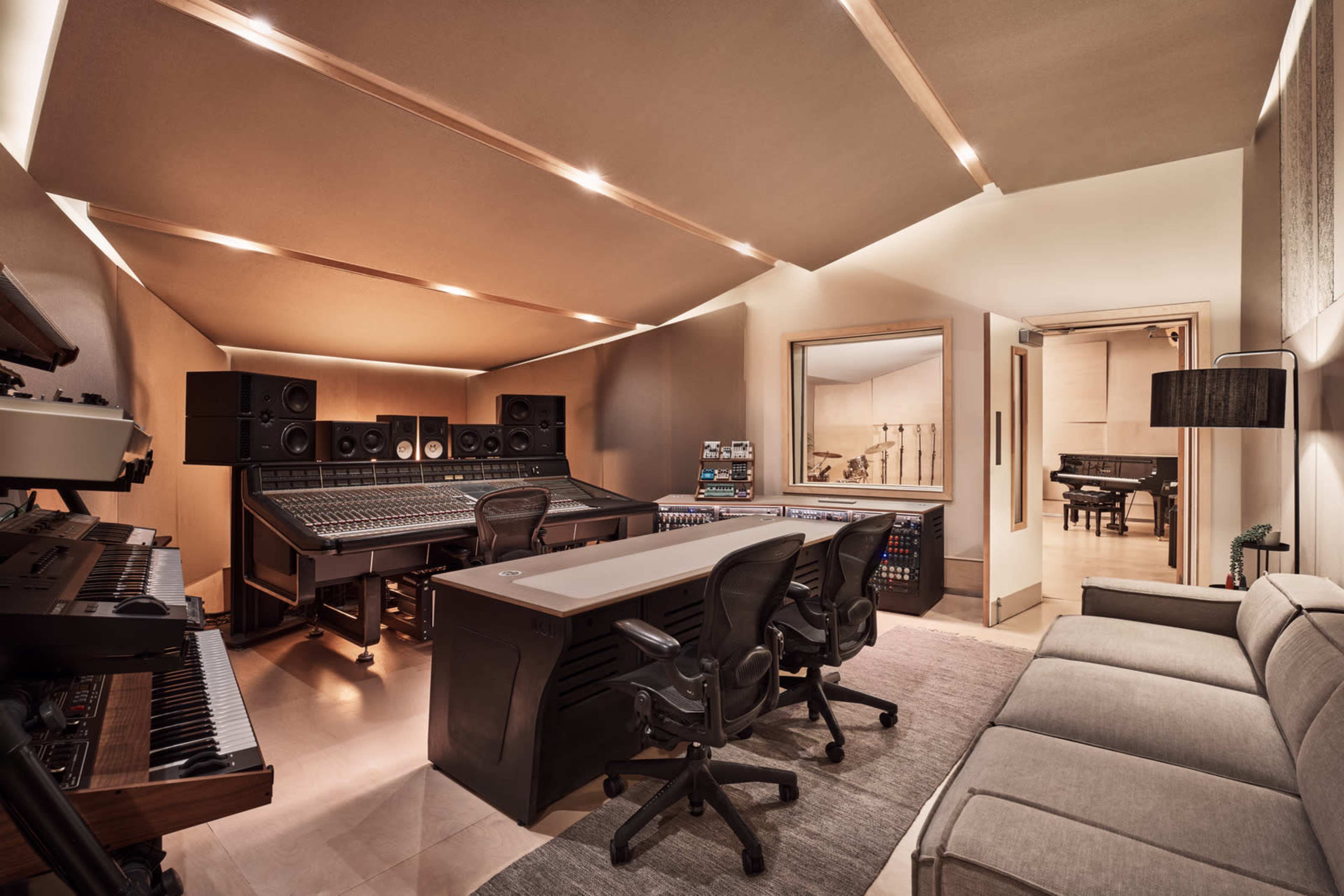 A modern music recording studio with a large mixing console, sound equipment, and a comfortable seating area.