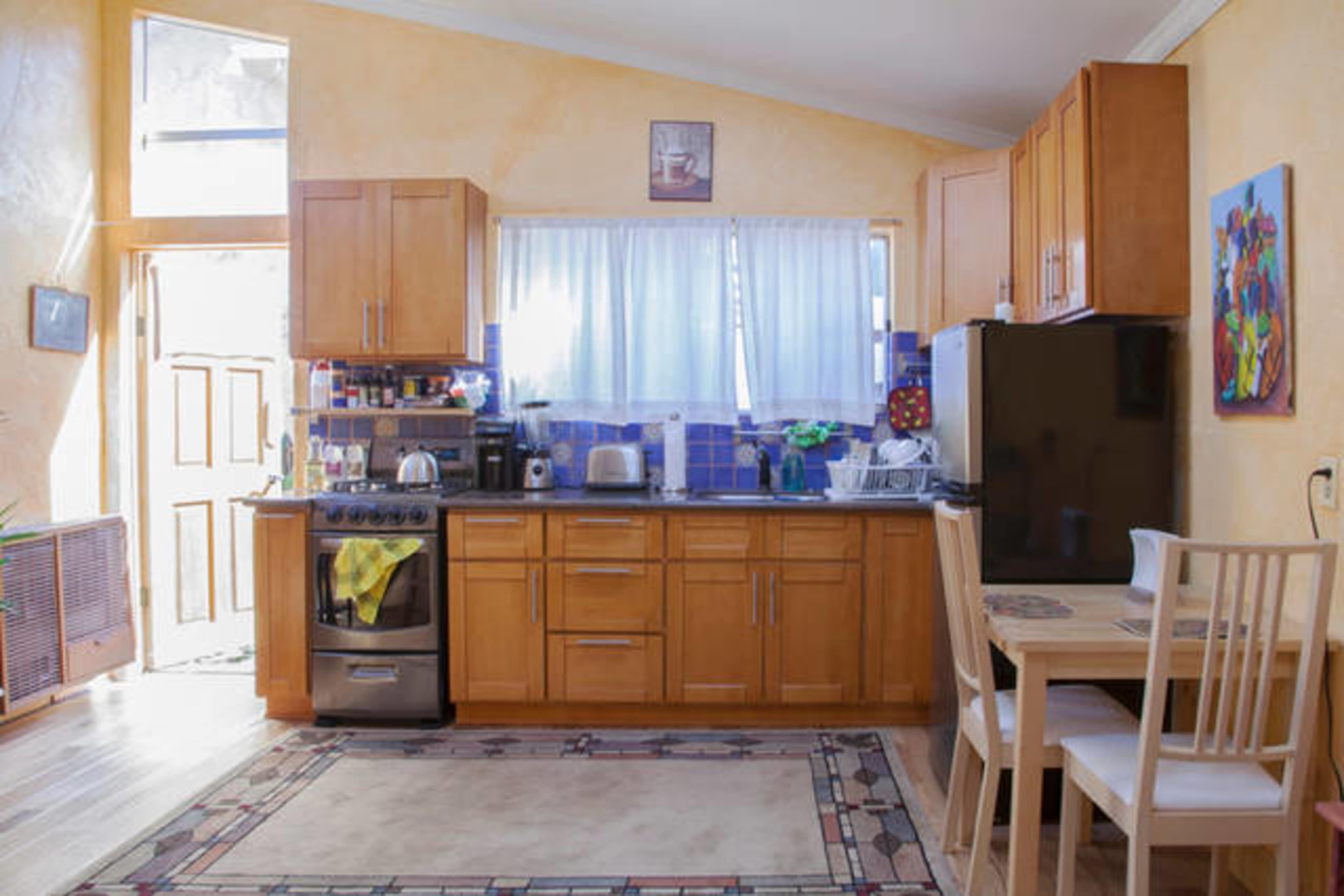 A kitchen with wooden cabinets, a stainless steel stove, and a small dining table in a well-lit space.