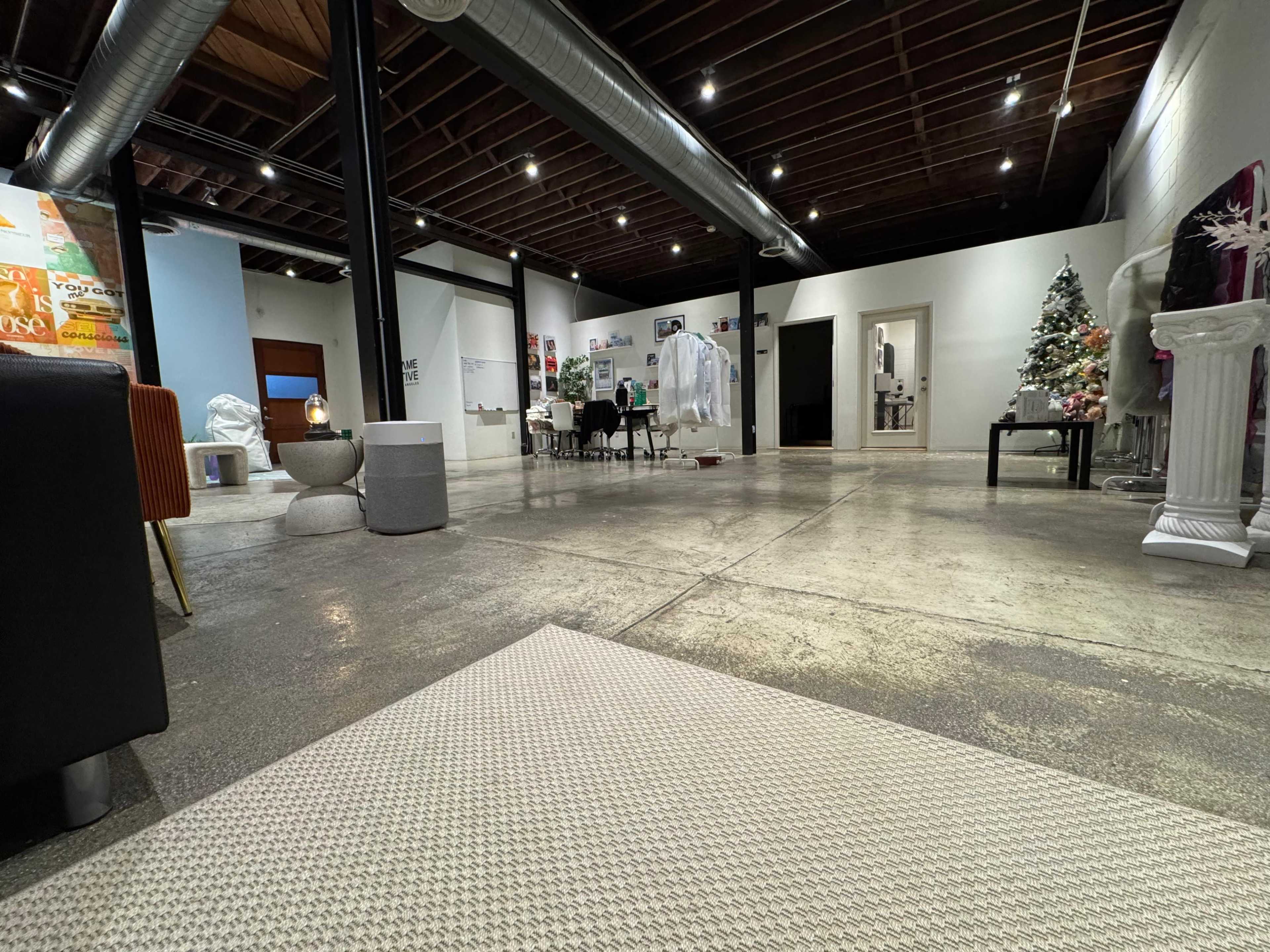 The image depicts a spacious, modern interior with polished concrete floors, various artworks on the walls, and a Christmas tree in the corner.