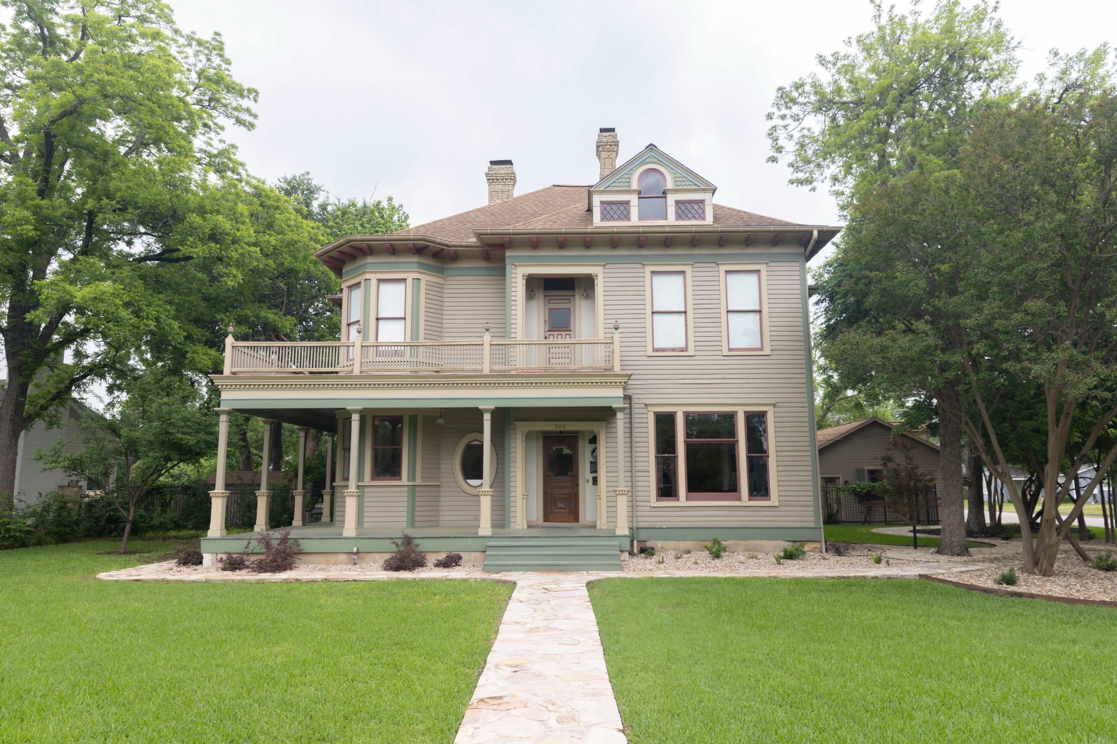 A large, two-story Victorian-style house with a wraparound porch and a neatly landscaped front yard.