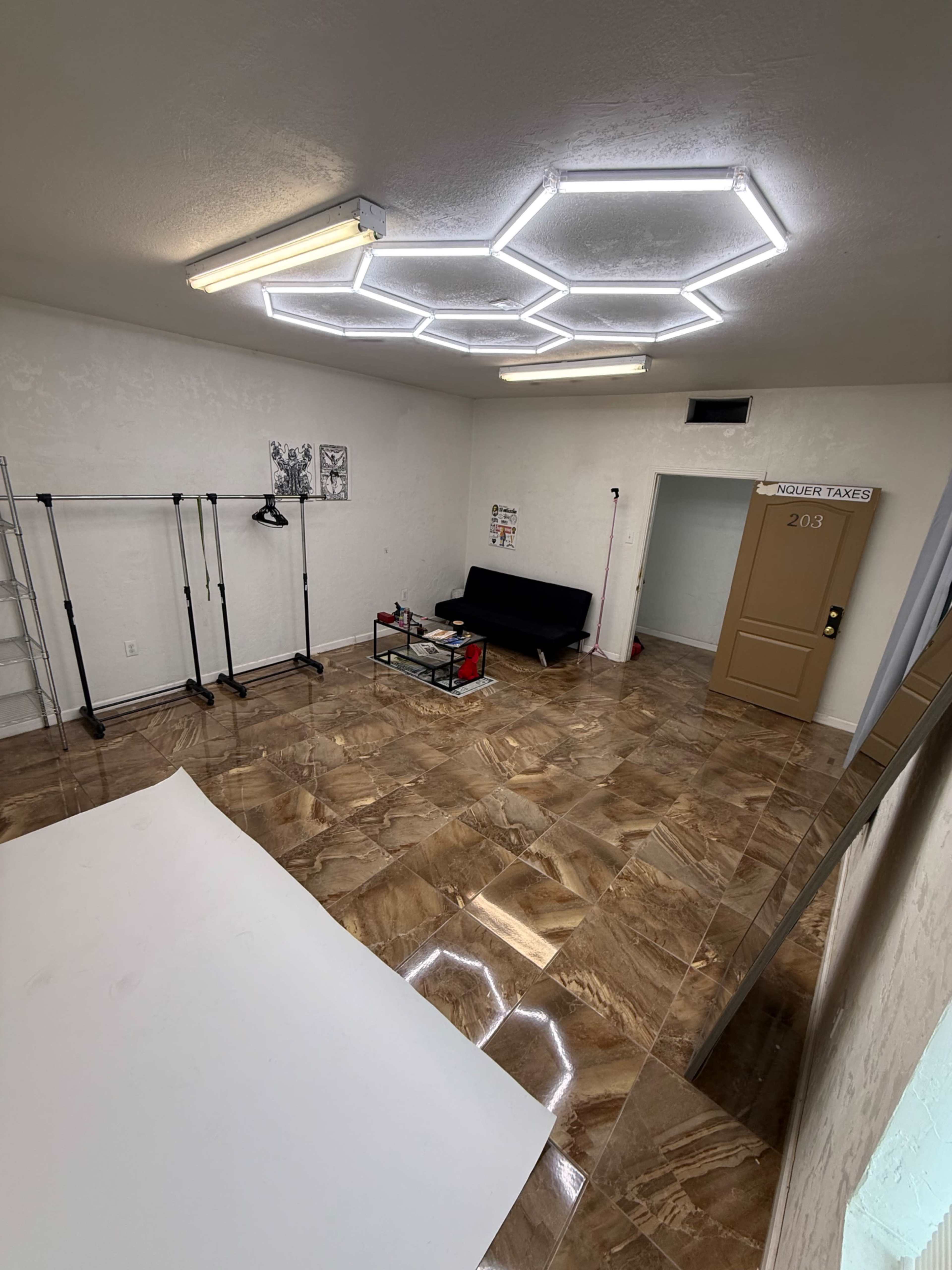 The image depicts a spacious room featuring a hexagonal LED light fixture, a black couch, a coffee table with a glass top, and minimalist decor on the walls.