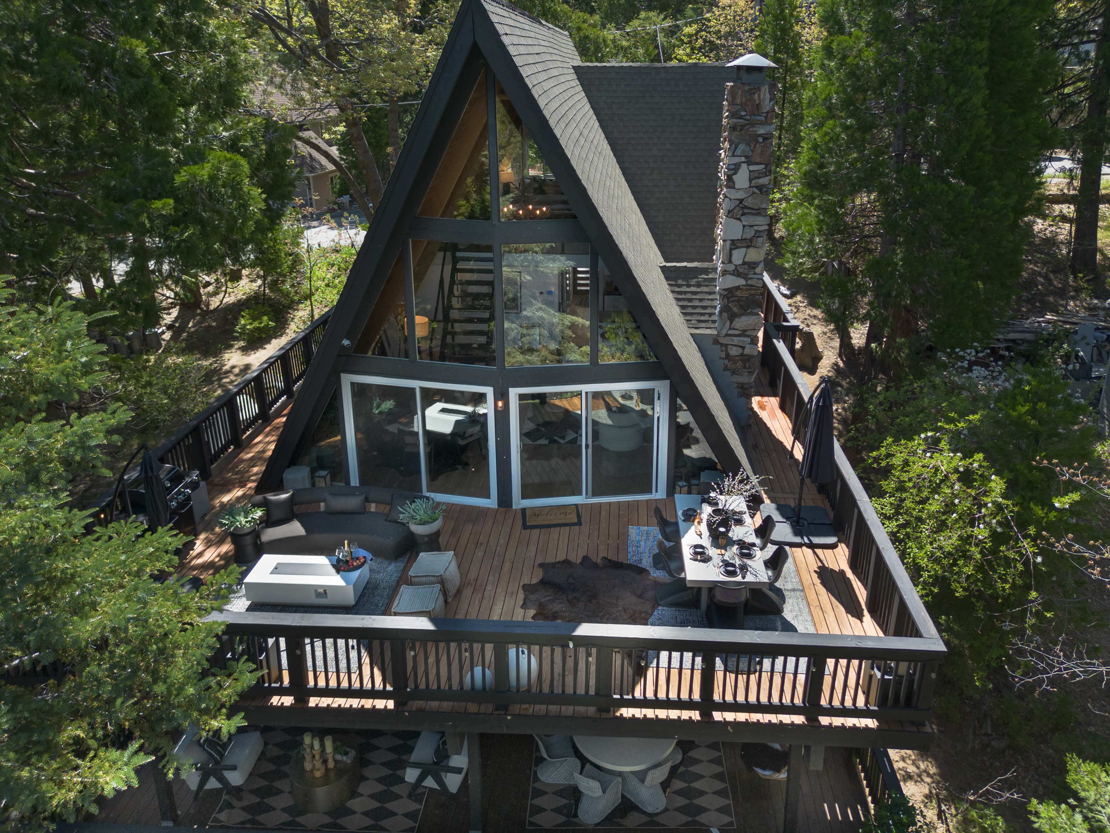 A modern A-frame cabin with large windows and a spacious deck surrounded by trees.