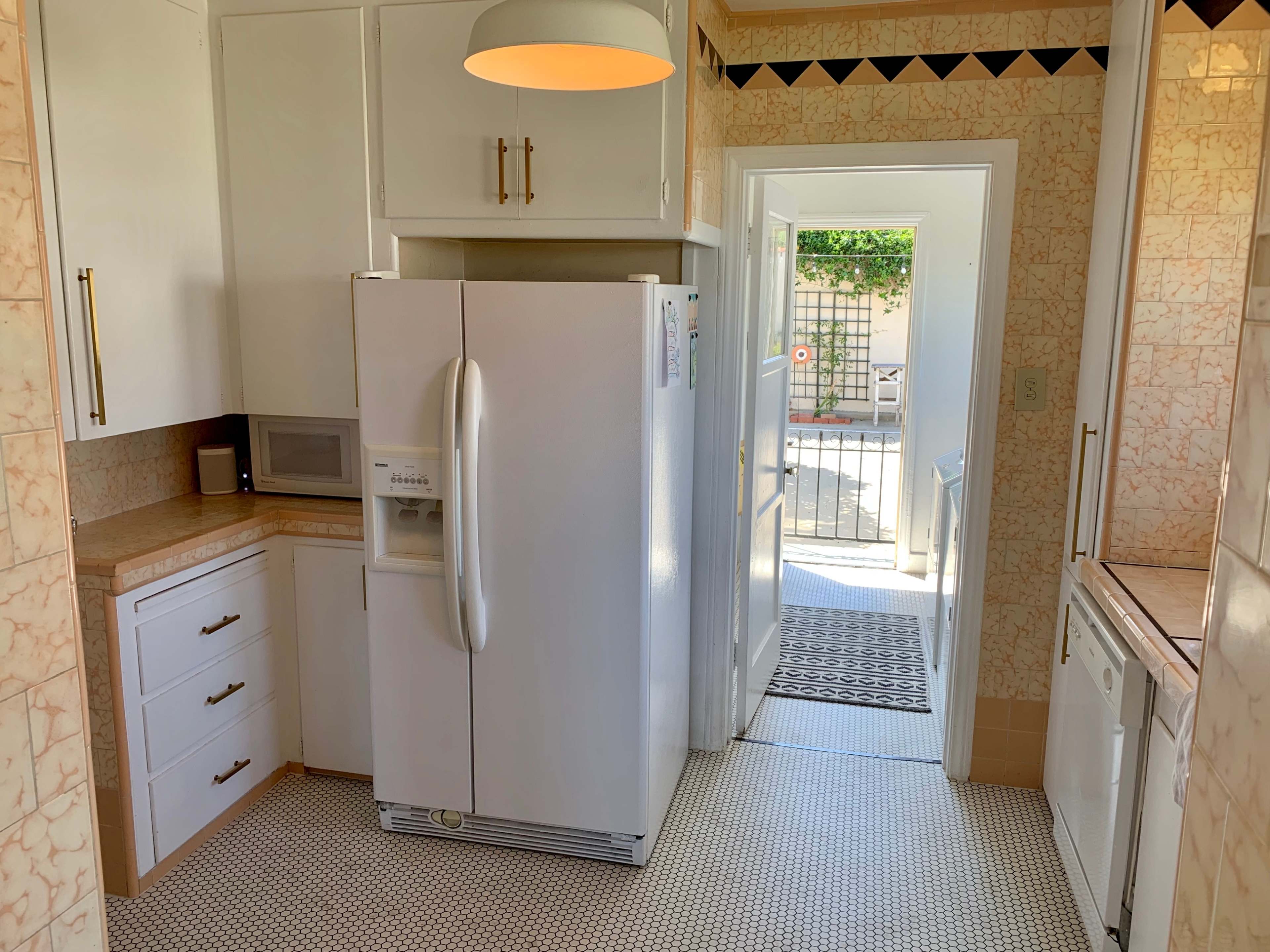 A kitchen with white appliances, including a refrigerator and microwave, along with light-colored countertops and tiled flooring.