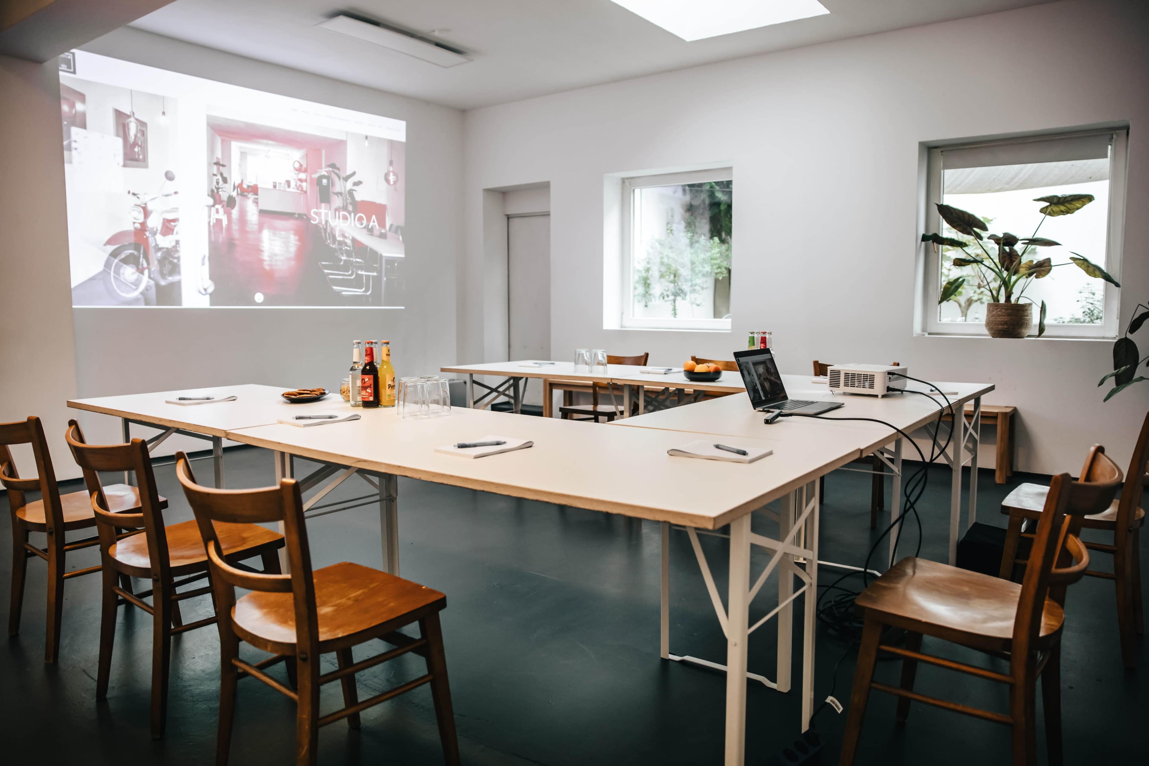 A modern meeting room features several tables and chairs arranged for a presentation, with a projector displaying an image on the wall.