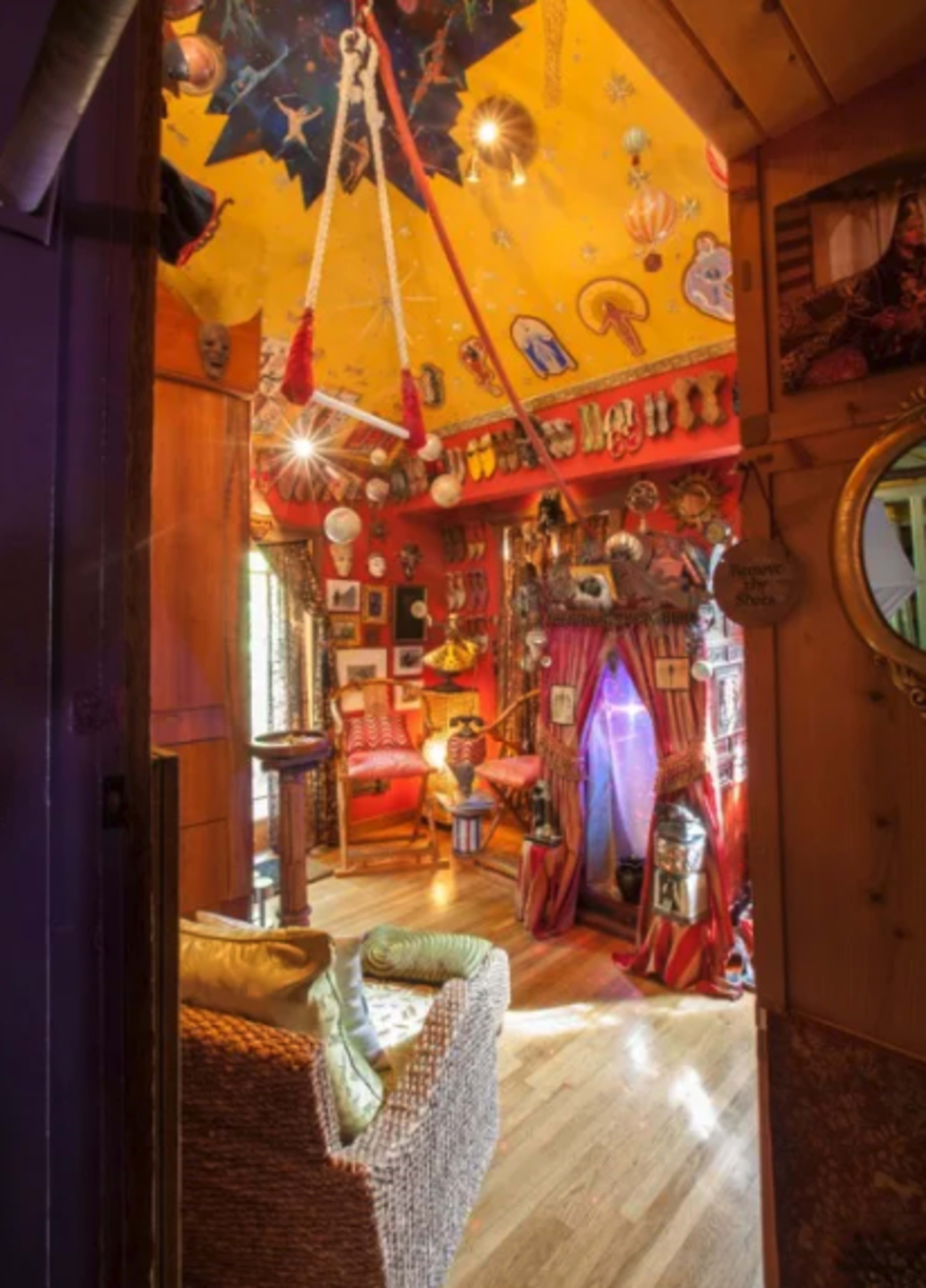 The image depicts a uniquely decorated room with a colorful ceiling, various art pieces adorning the walls, and a cozy seating area.