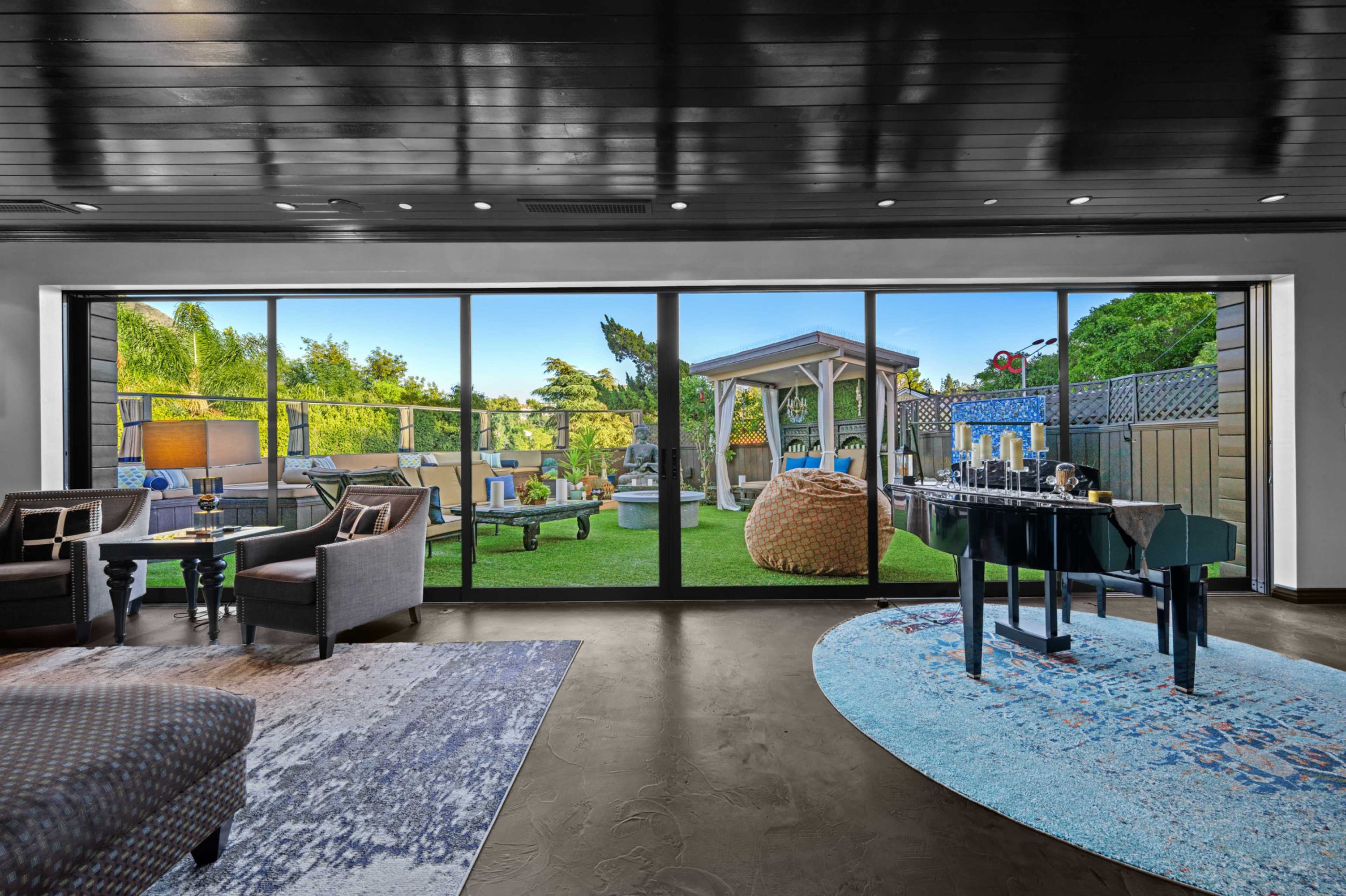 A modern living room with large windows overlooking a backyard featuring a gazebo and outdoor seating.