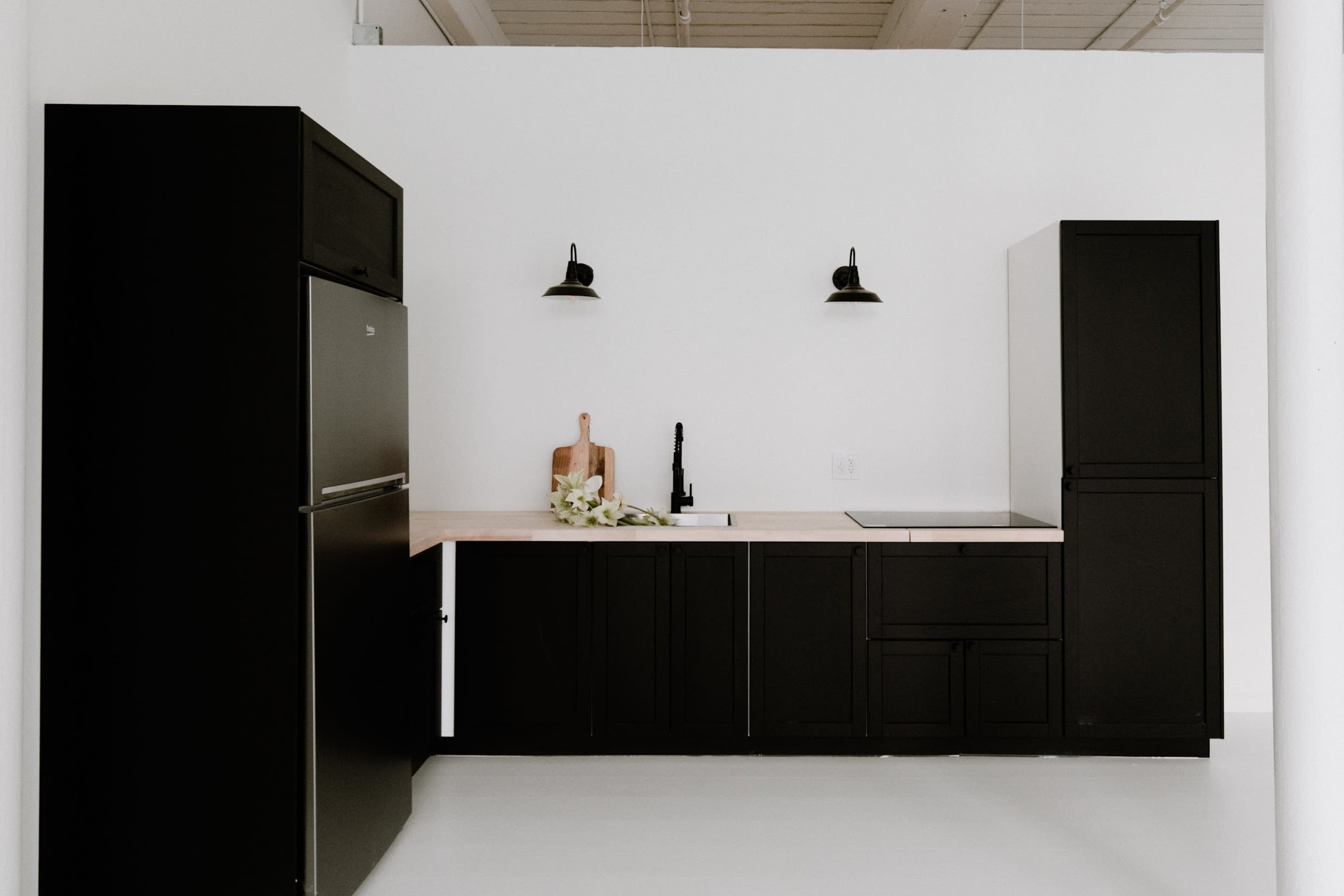 A modern kitchen with black cabinetry, a wooden countertop, and minimalistic lighting.