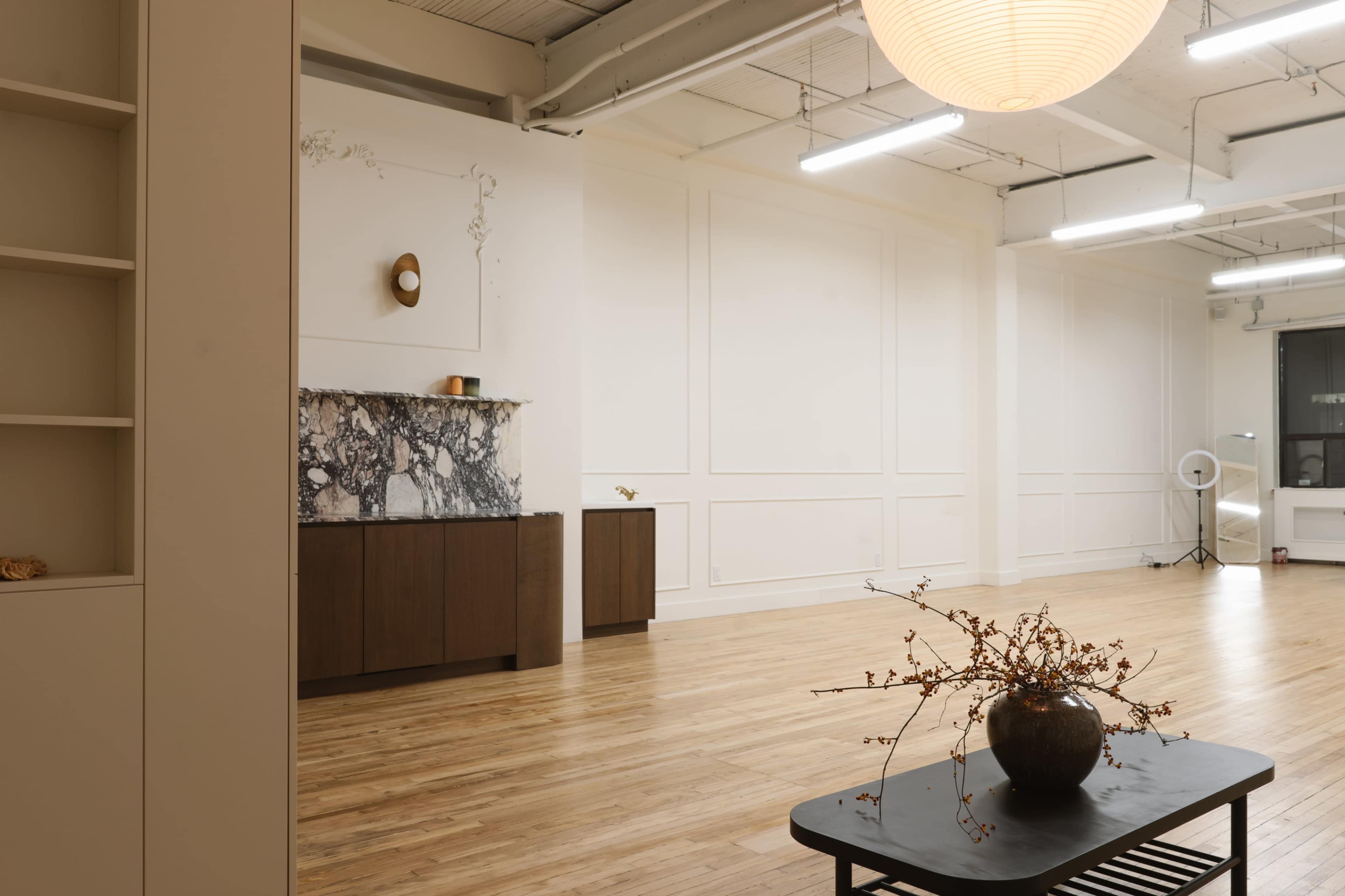 A spacious interior features light wooden floors, minimalist furniture, and a marble fireplace against a white wall.