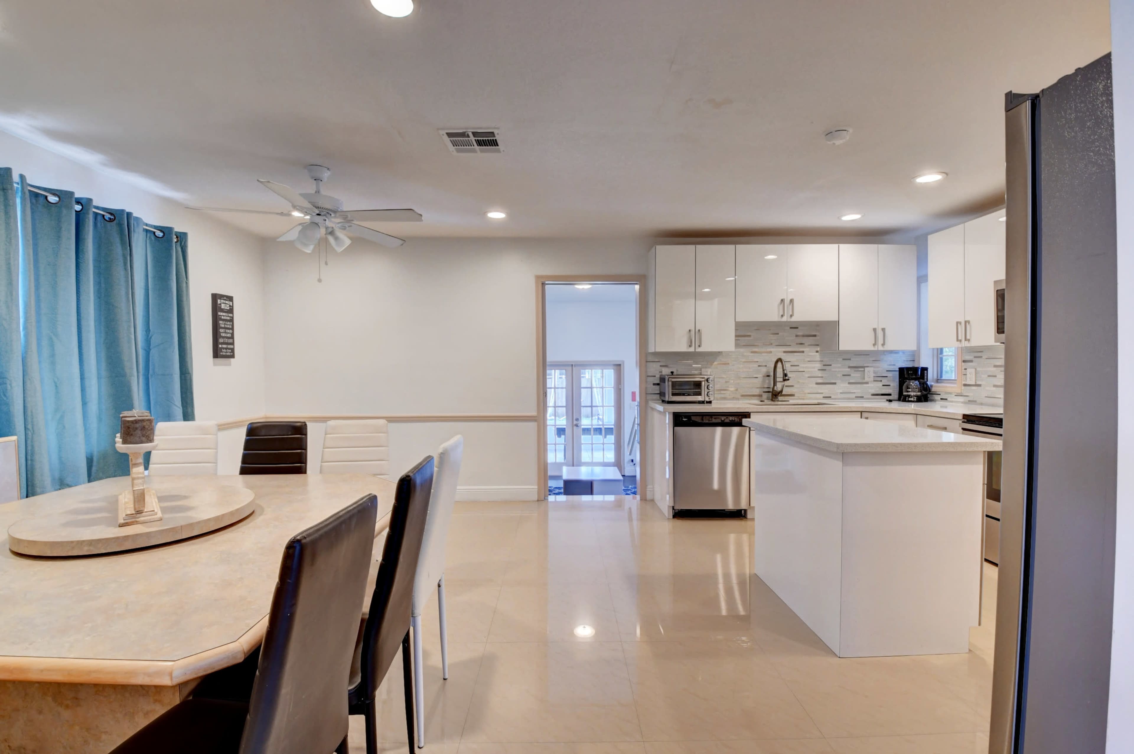 The image shows a modern kitchen and dining area featuring a round dining table and sleek cabinetry with stainless steel appliances.