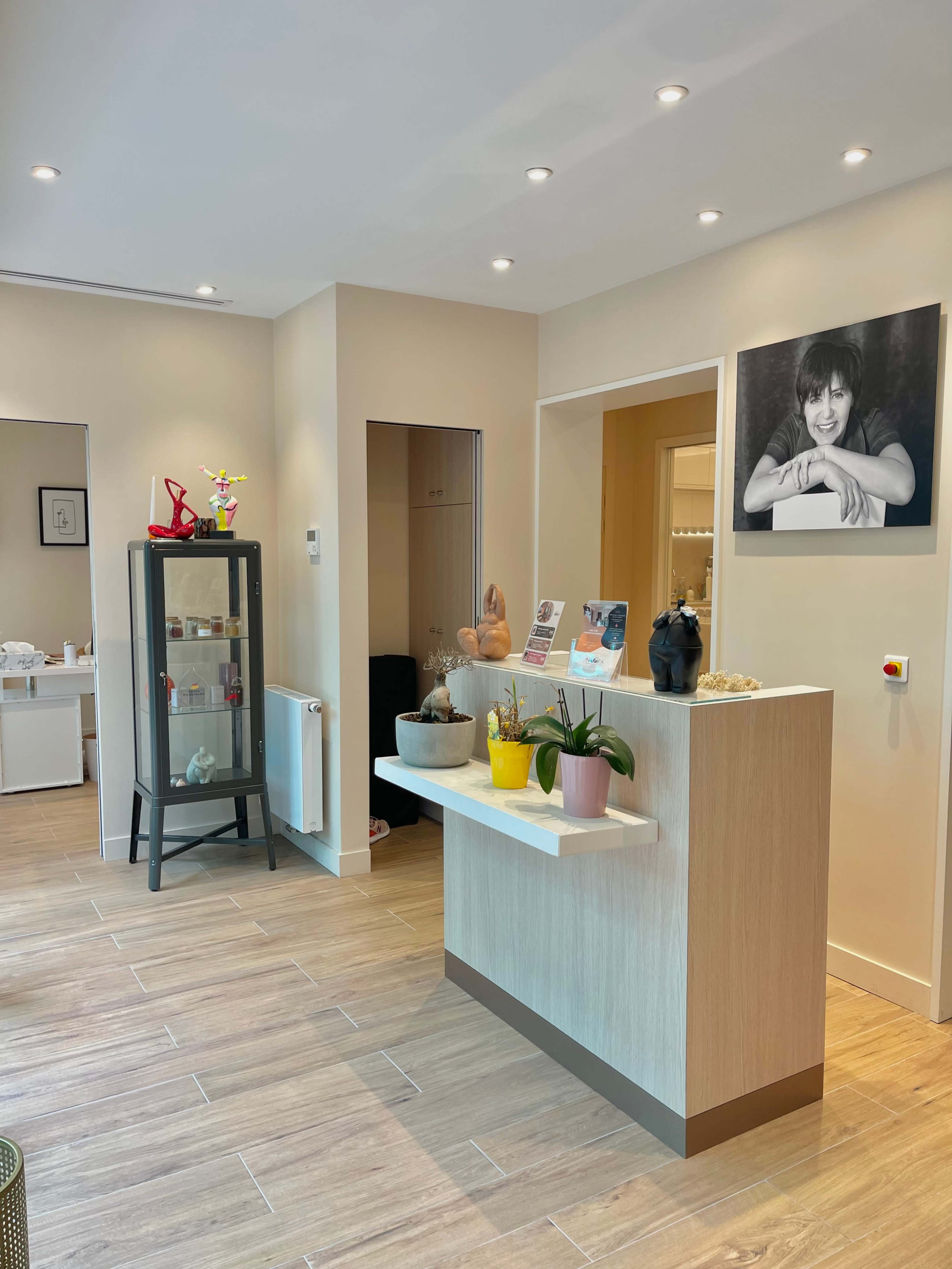 A well-lit reception area featuring a display cabinet, a counter with potted plants, and a framed portrait on the wall.