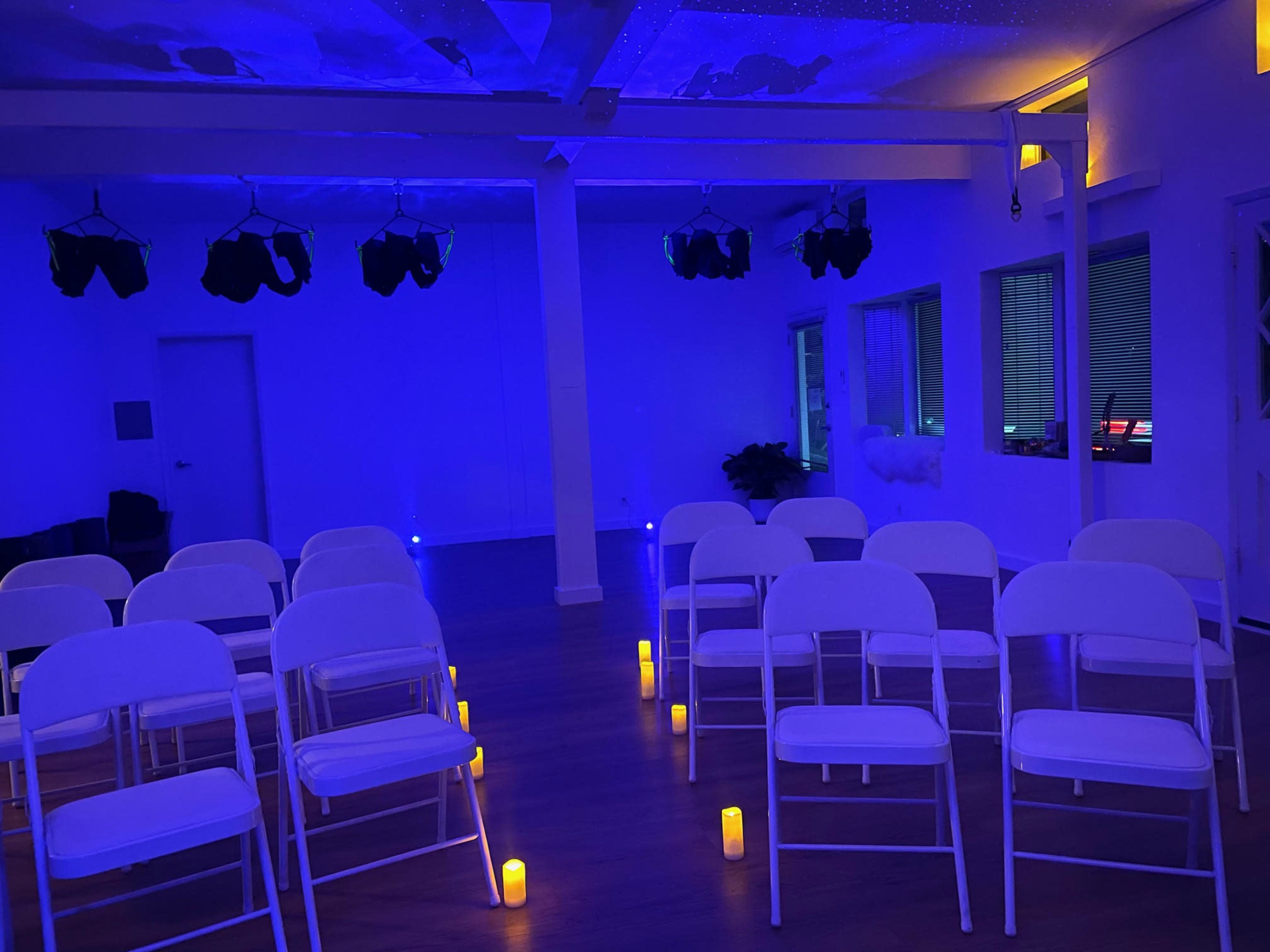 A brightly lit room with white chairs arranged in rows and illuminated by artificial candles on the floor.