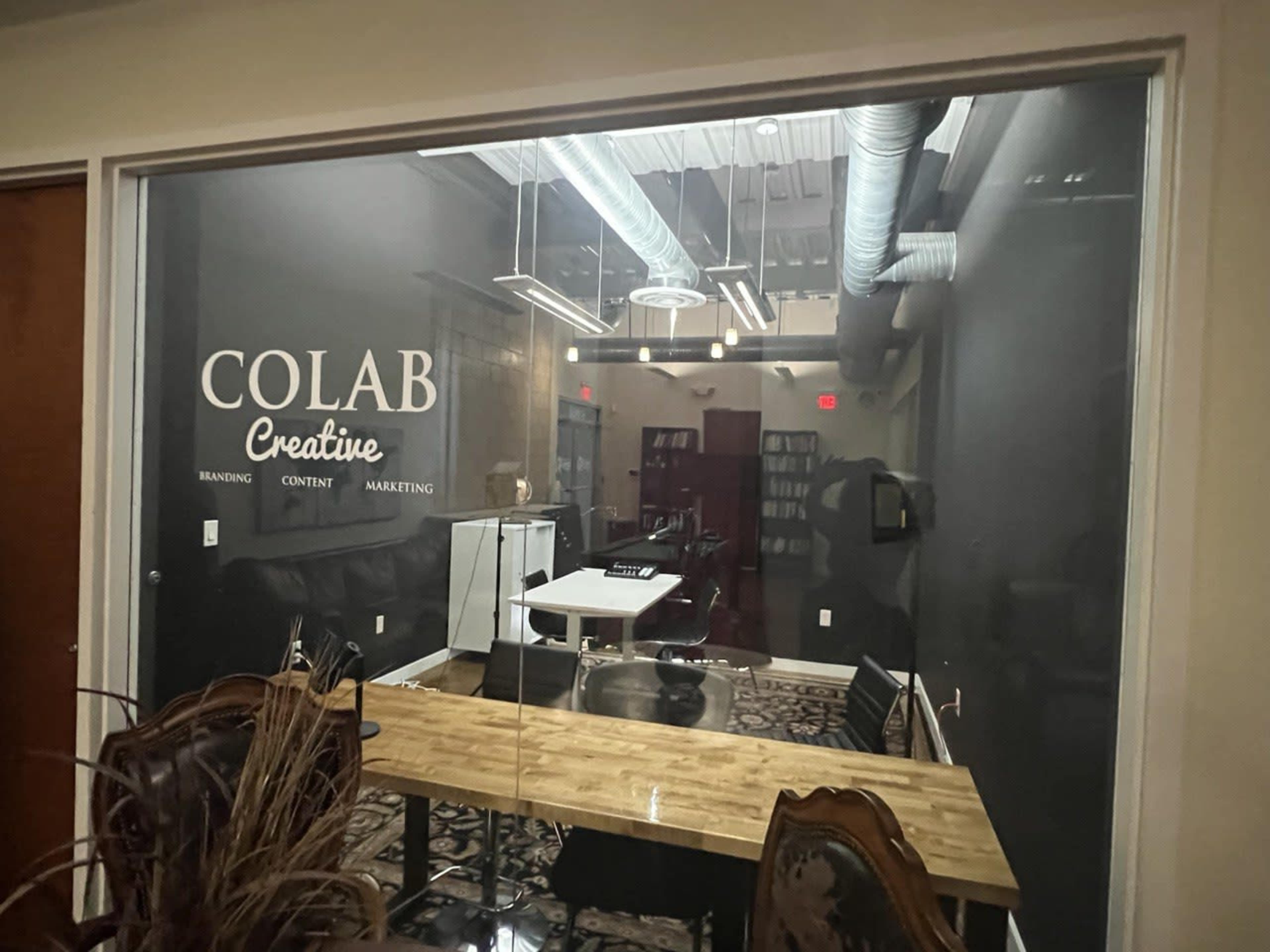 A modern office space labeled "COLAB Creative," featuring a wooden table, a black wall, and equipment for branding, content, and marketing.