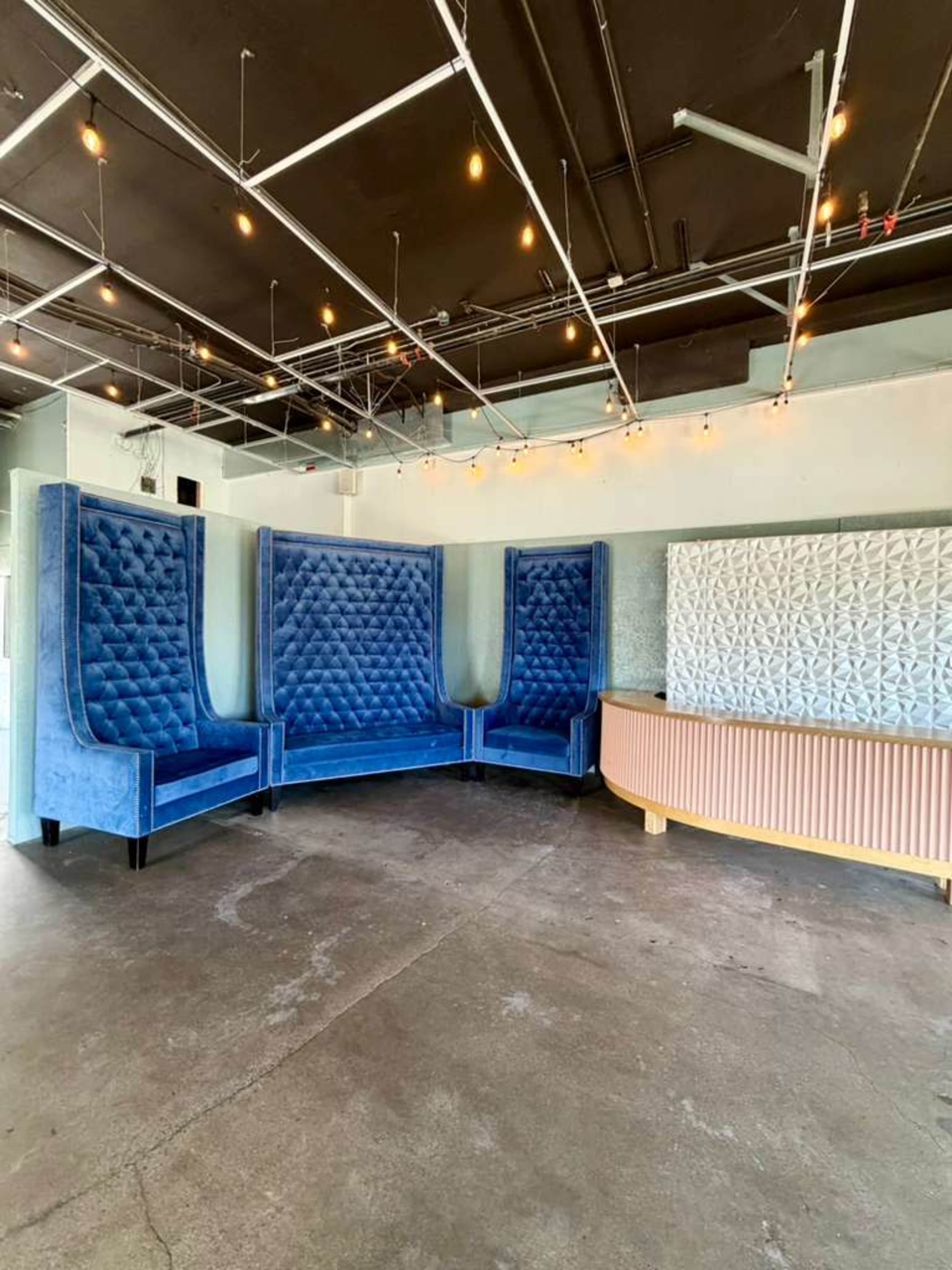 The image shows a spacious interior with blue velvet booths and a wooden reception desk against a lightly decorated wall.