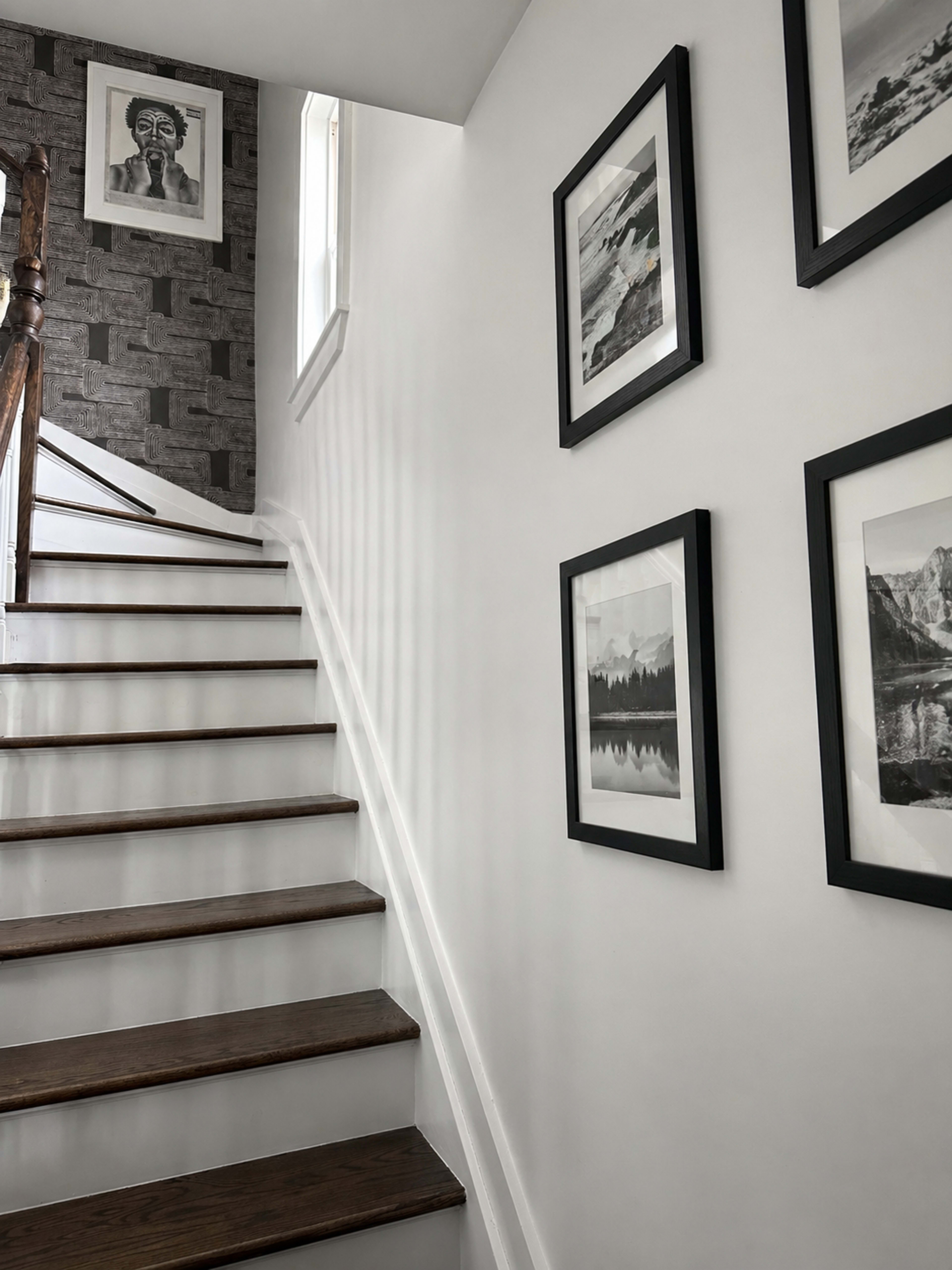 The image shows a staircase leading upward, with framed black-and-white photographs on the wall and a patterned accent wall at the top.