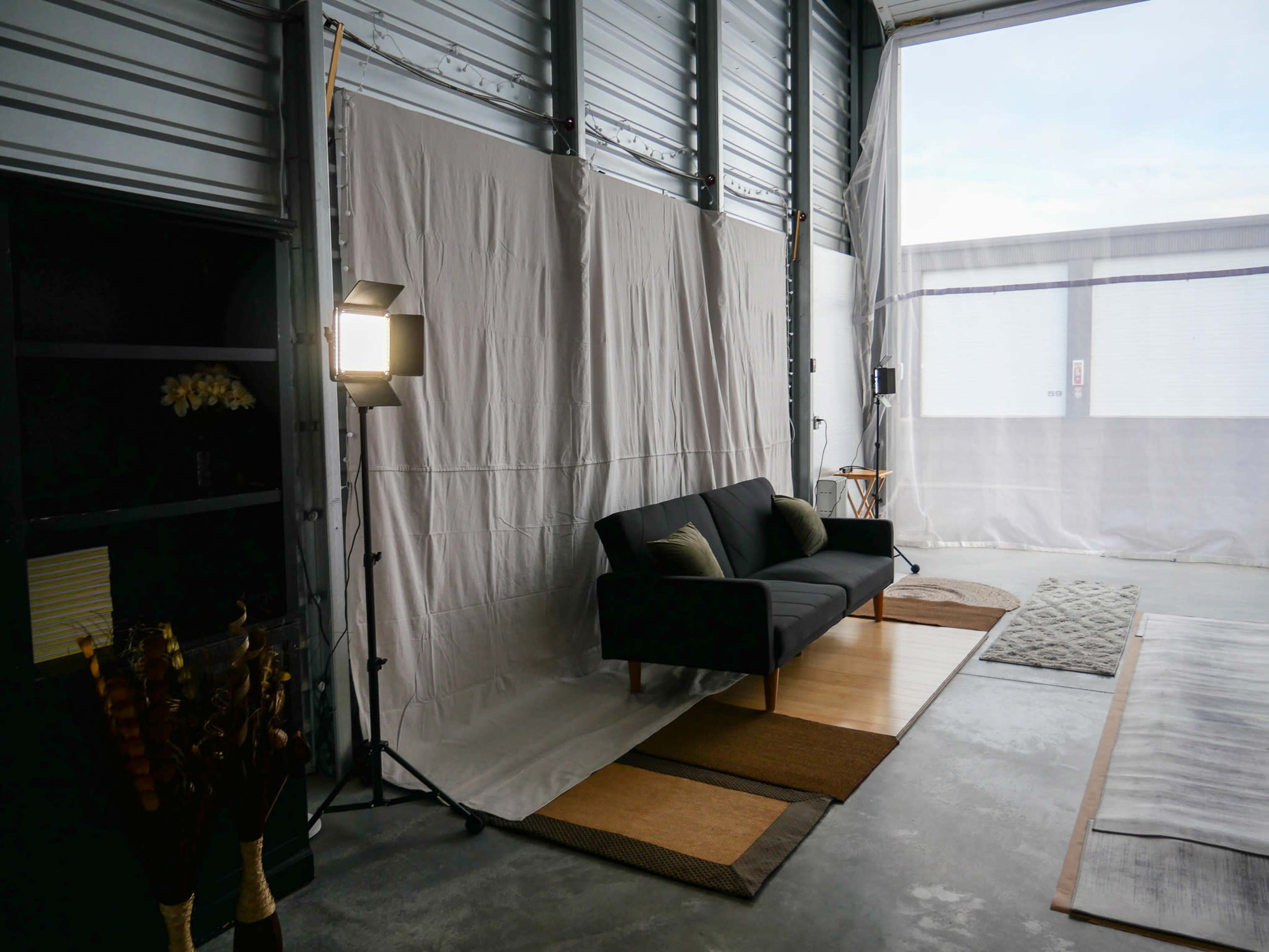A modern indoor space features a black sofa against a white backdrop, with various textures on the floor and a light source illuminating the area.