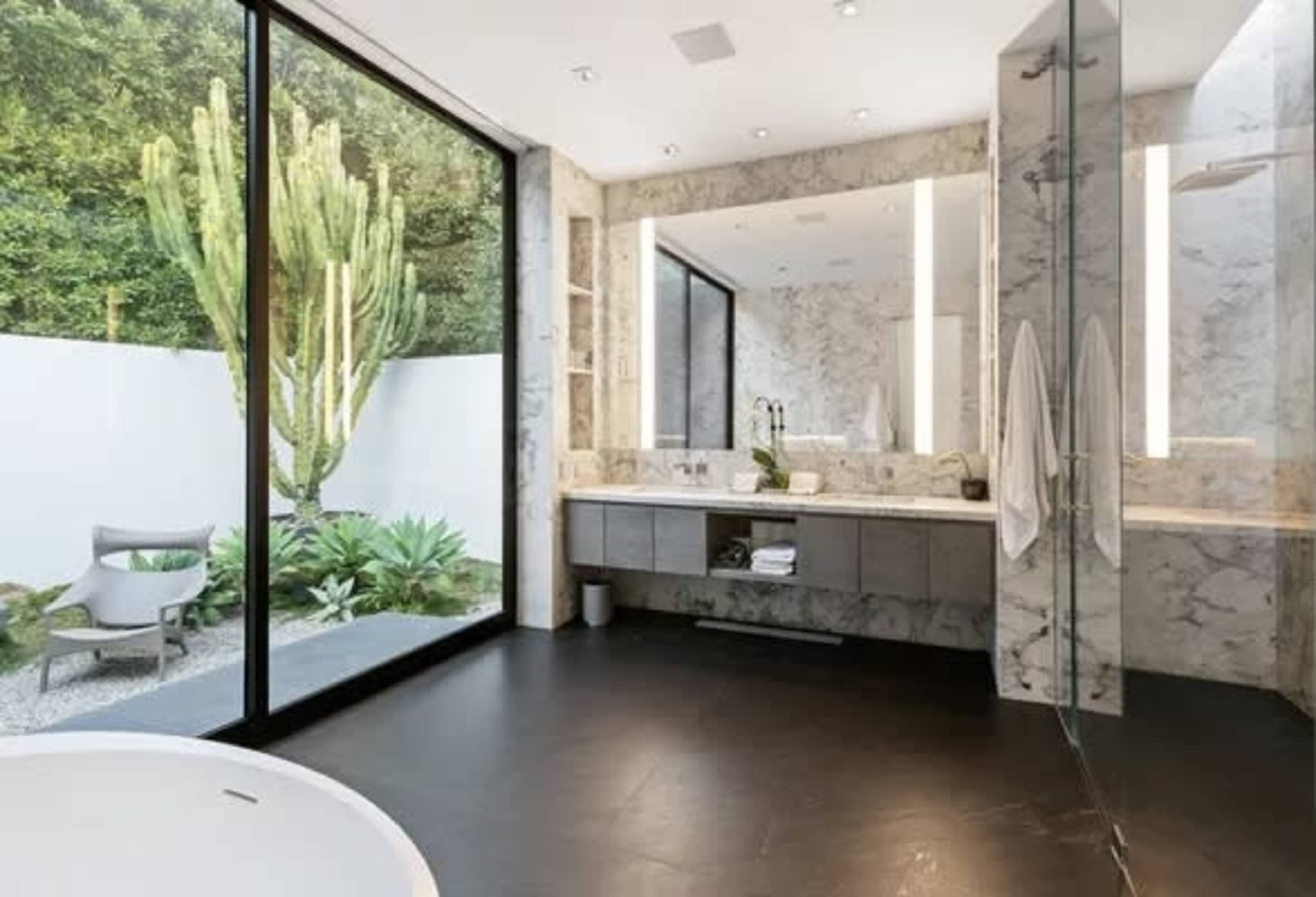 The bathroom features a large window with a view of a cactus garden, a contemporary double sink vanity, and a freestanding bathtub.