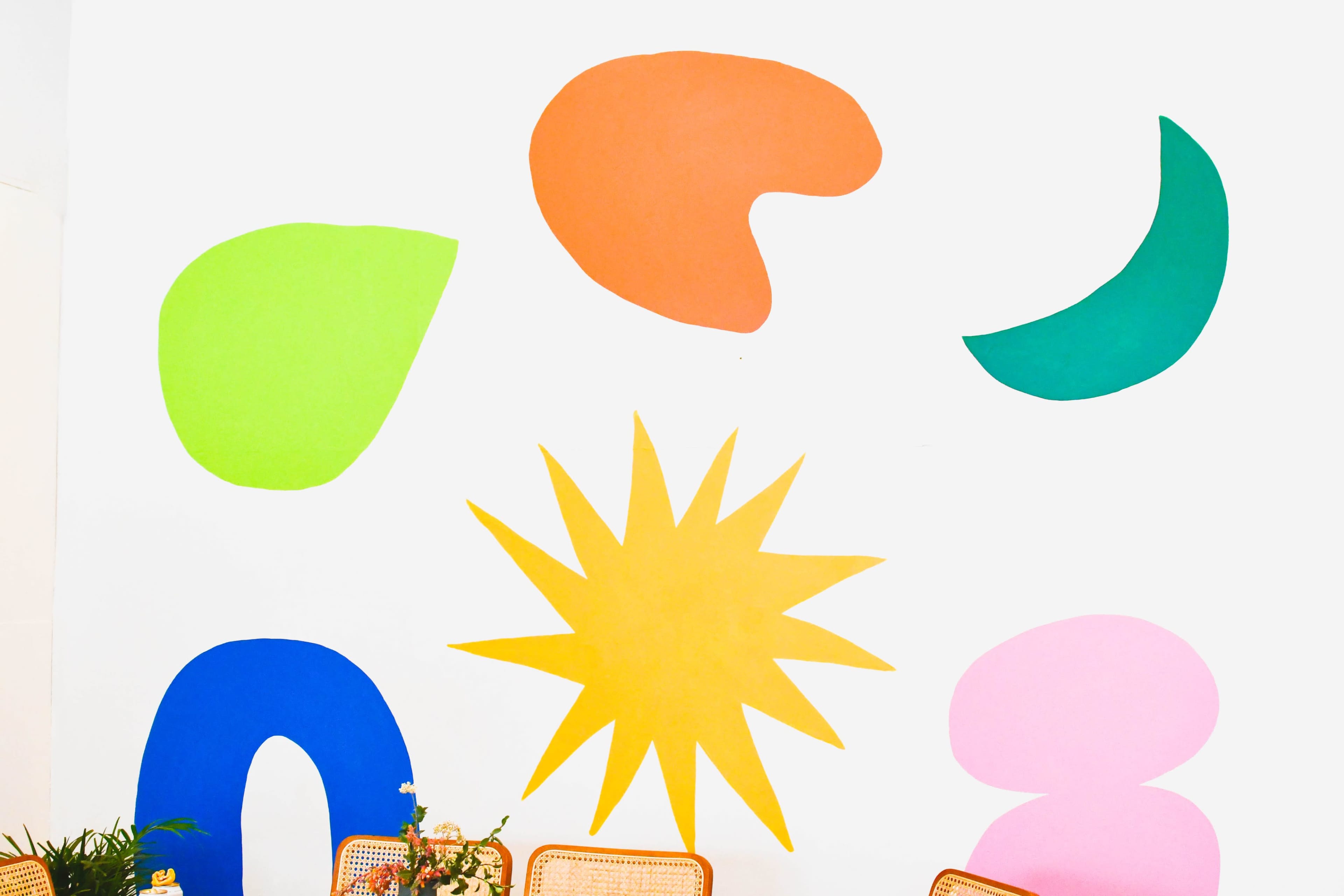 The image features a brightly colored mural on a white wall, displaying various abstract shapes in green, orange, blue, yellow, and pink.