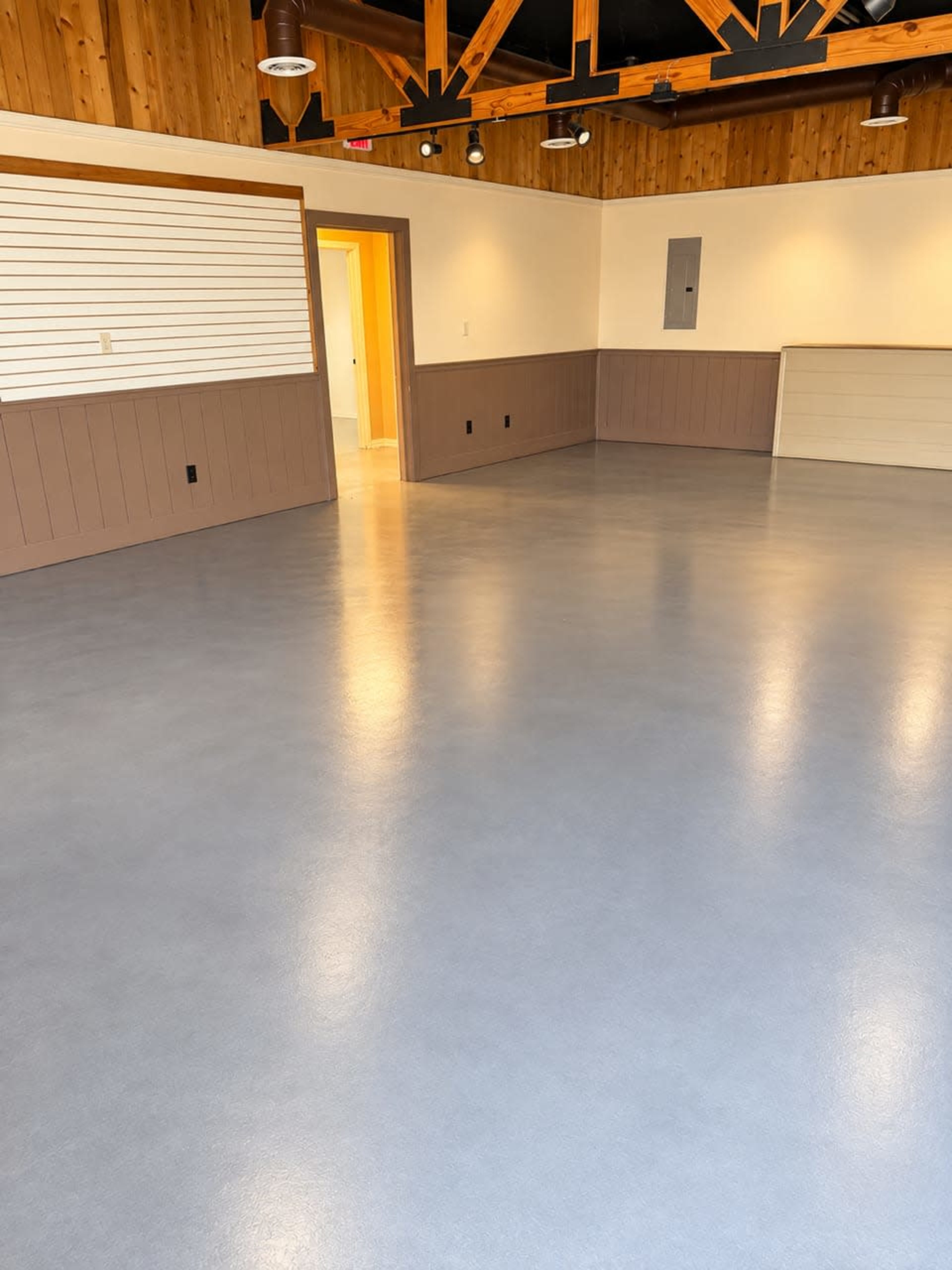 The image shows an empty room with a polished gray floor, wooden walls, and a ceiling featuring exposed beams.