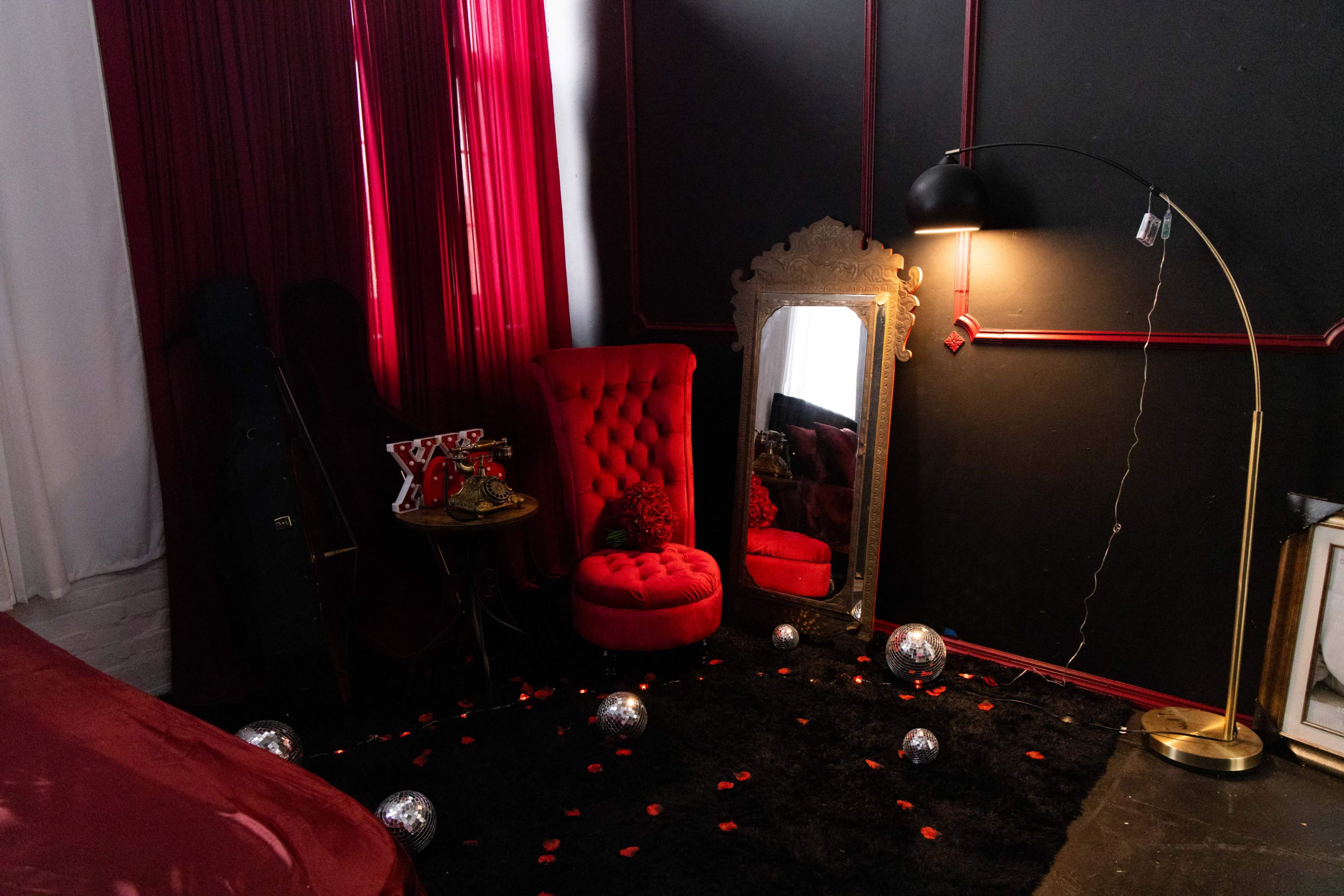 The scene features a stylish corner of a room with a red velvet chair, a decorative mirror, a floor lamp, and scattered disco balls on a dark rug.