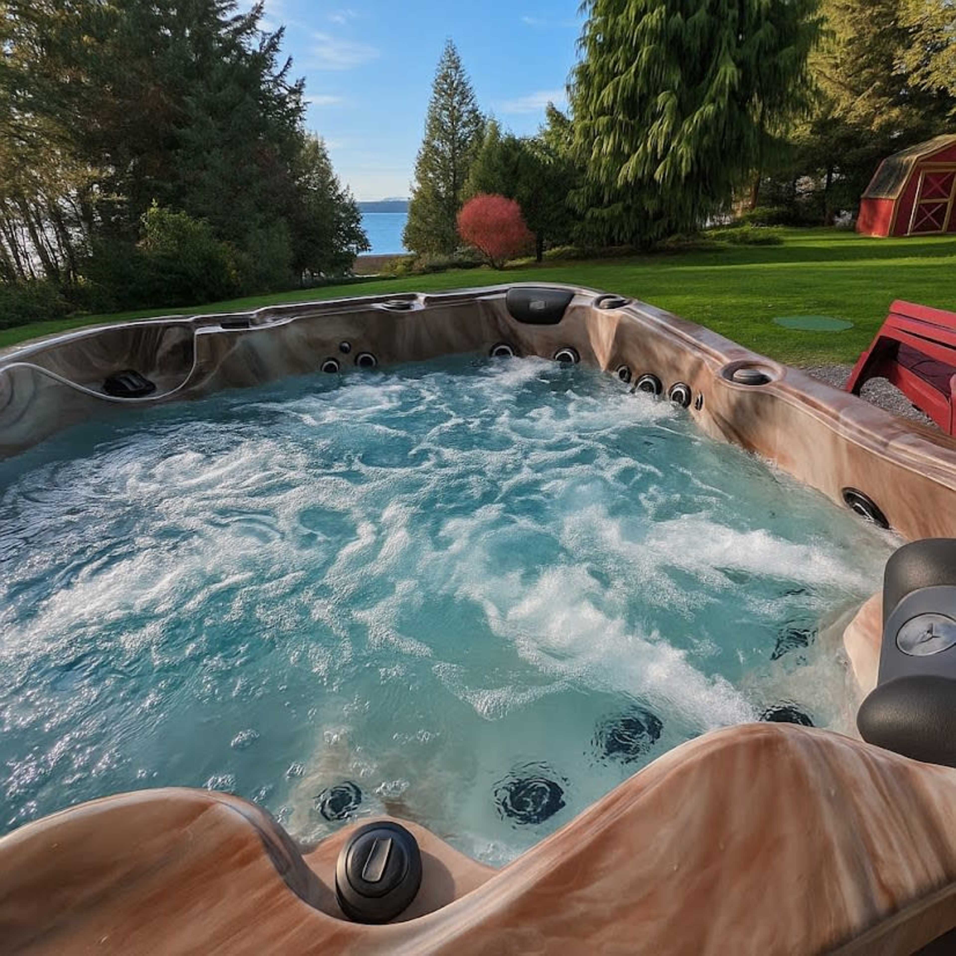 The image shows a hot tub filled with bubbling water, set in a lush green garden overlooking a body of water and surrounded by trees.