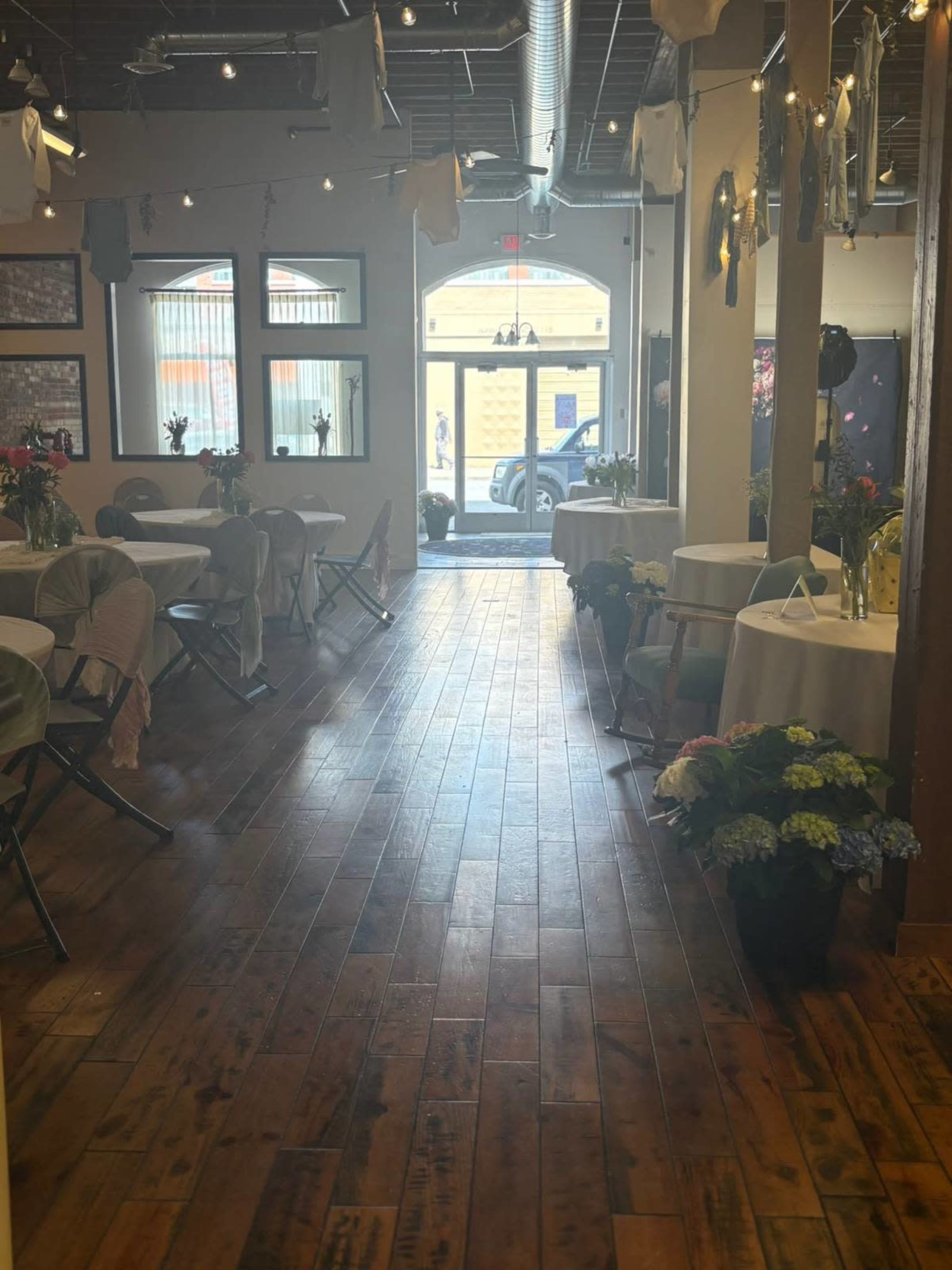 The image shows a large room with wooden floors, decorated tables, and a doorway leading to the street.